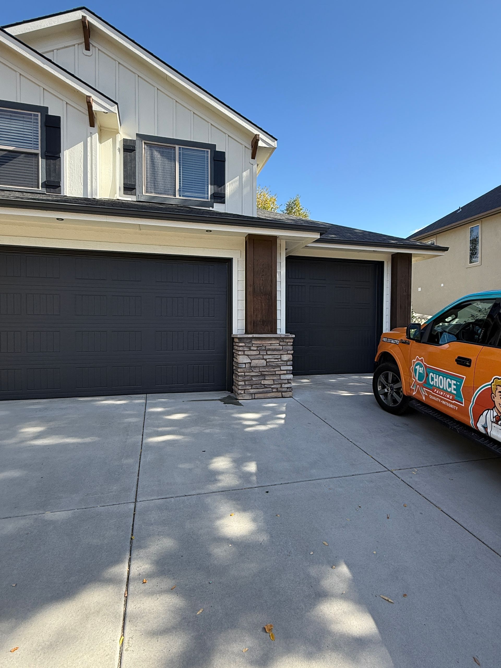 Suburban house with two black garage doors and an orange car parked in the driveway