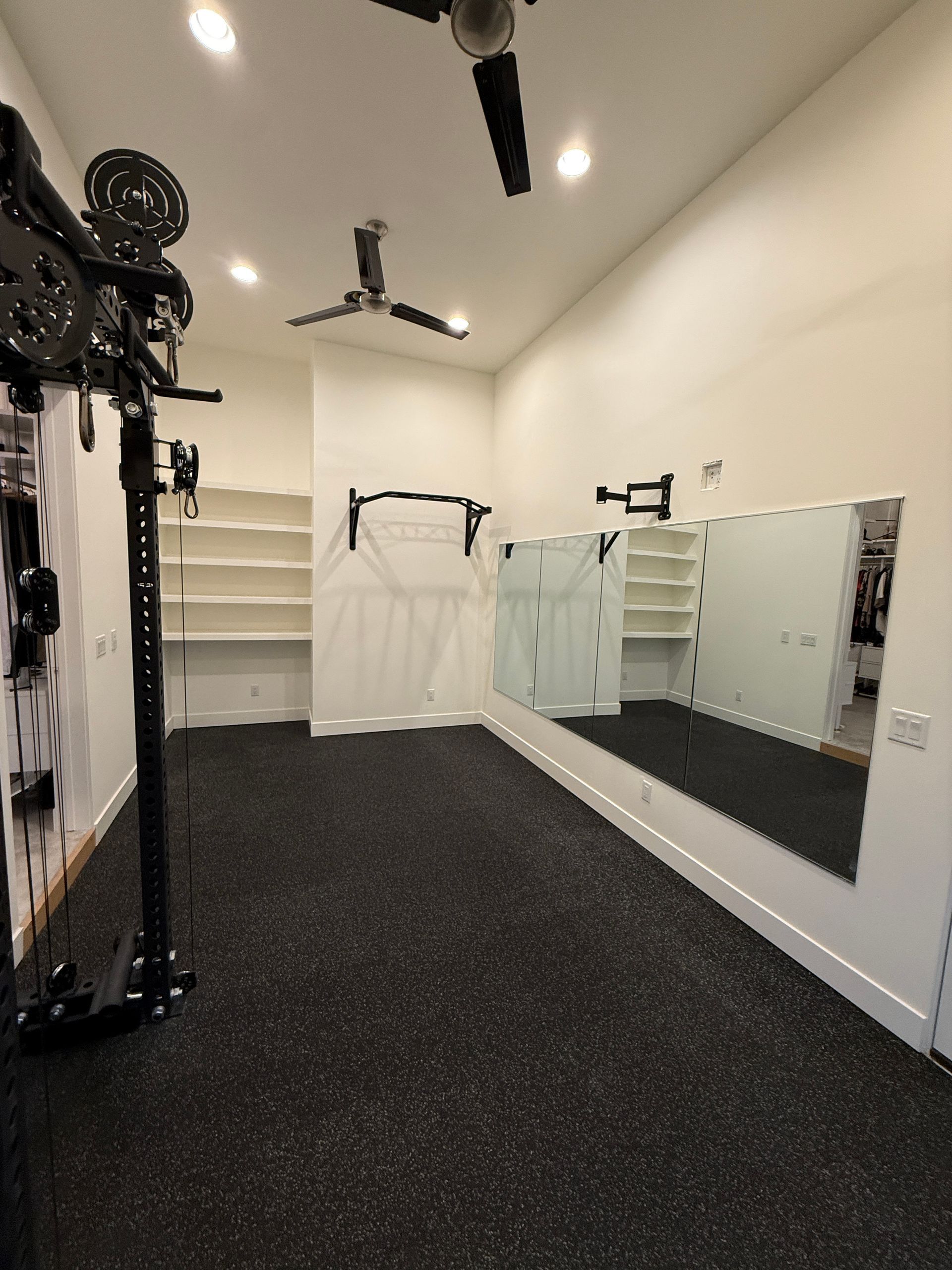 Empty gym studio with white walls, mirrors, black flooring, shelves, and ceiling fans