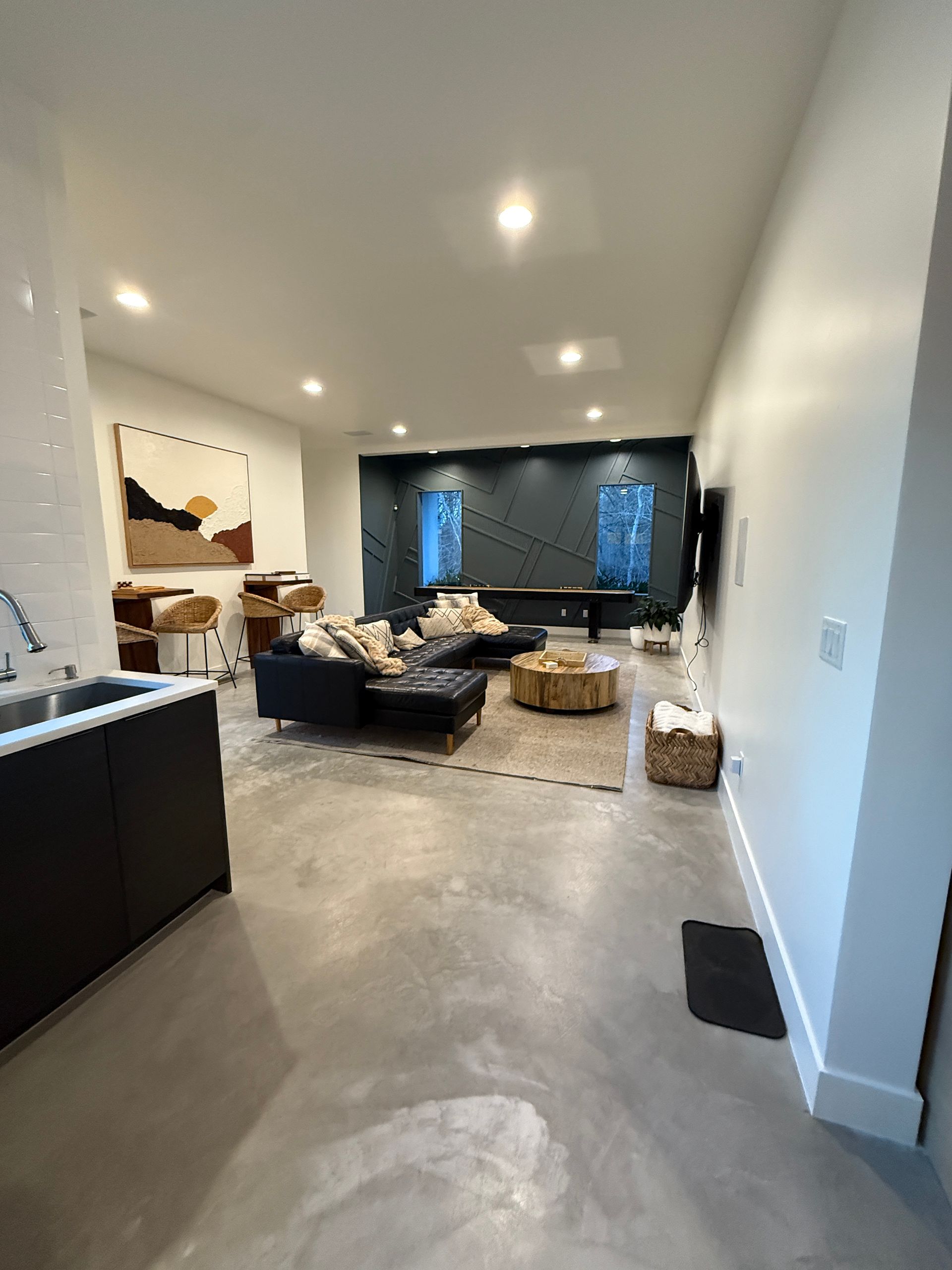 Modern living room with dark sofa, ottoman, large windows, and recessed ceiling lights