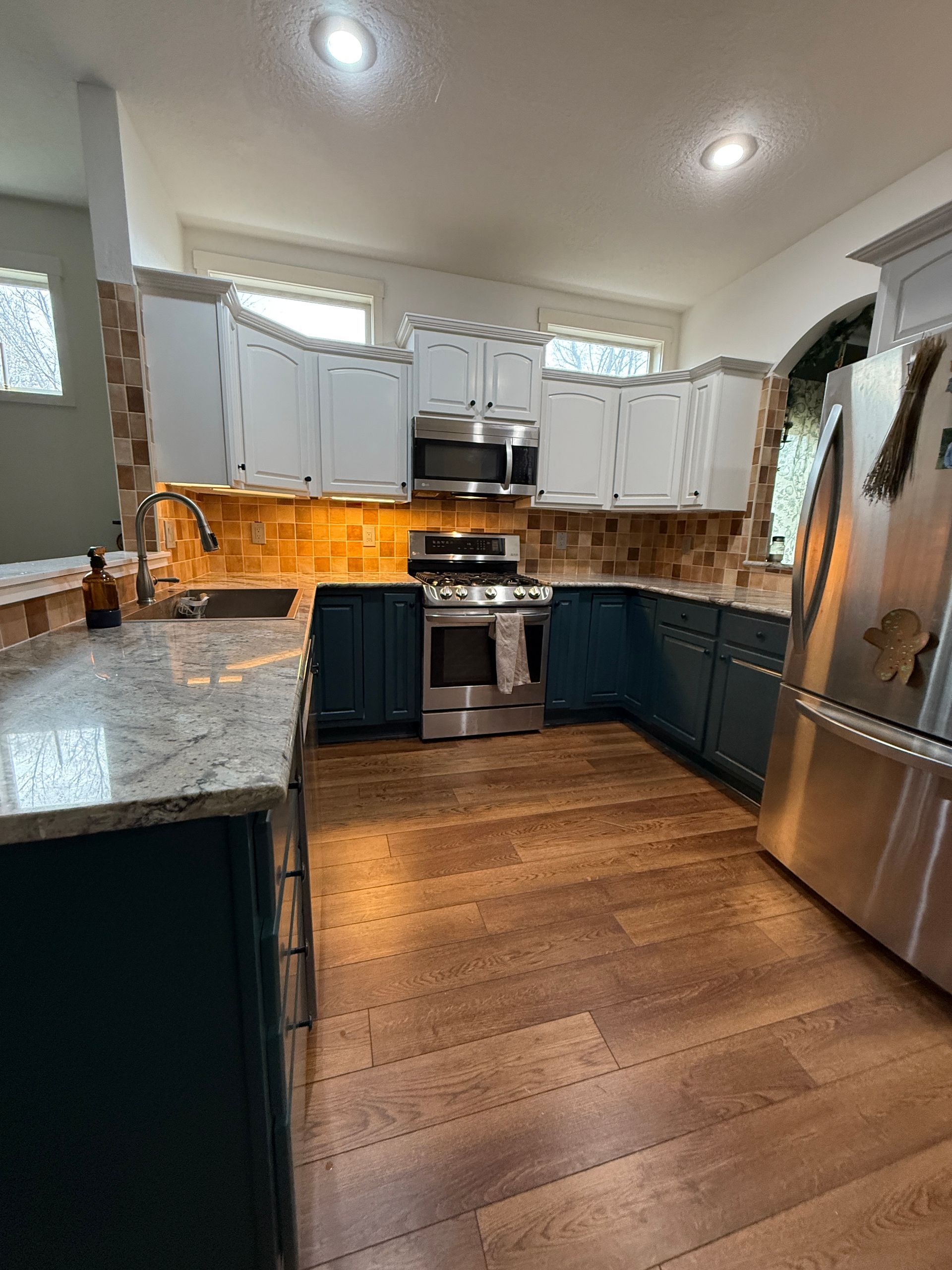 Modern kitchen with white cabinets, granite counters, stainless steel appliances, and warm wood flooring