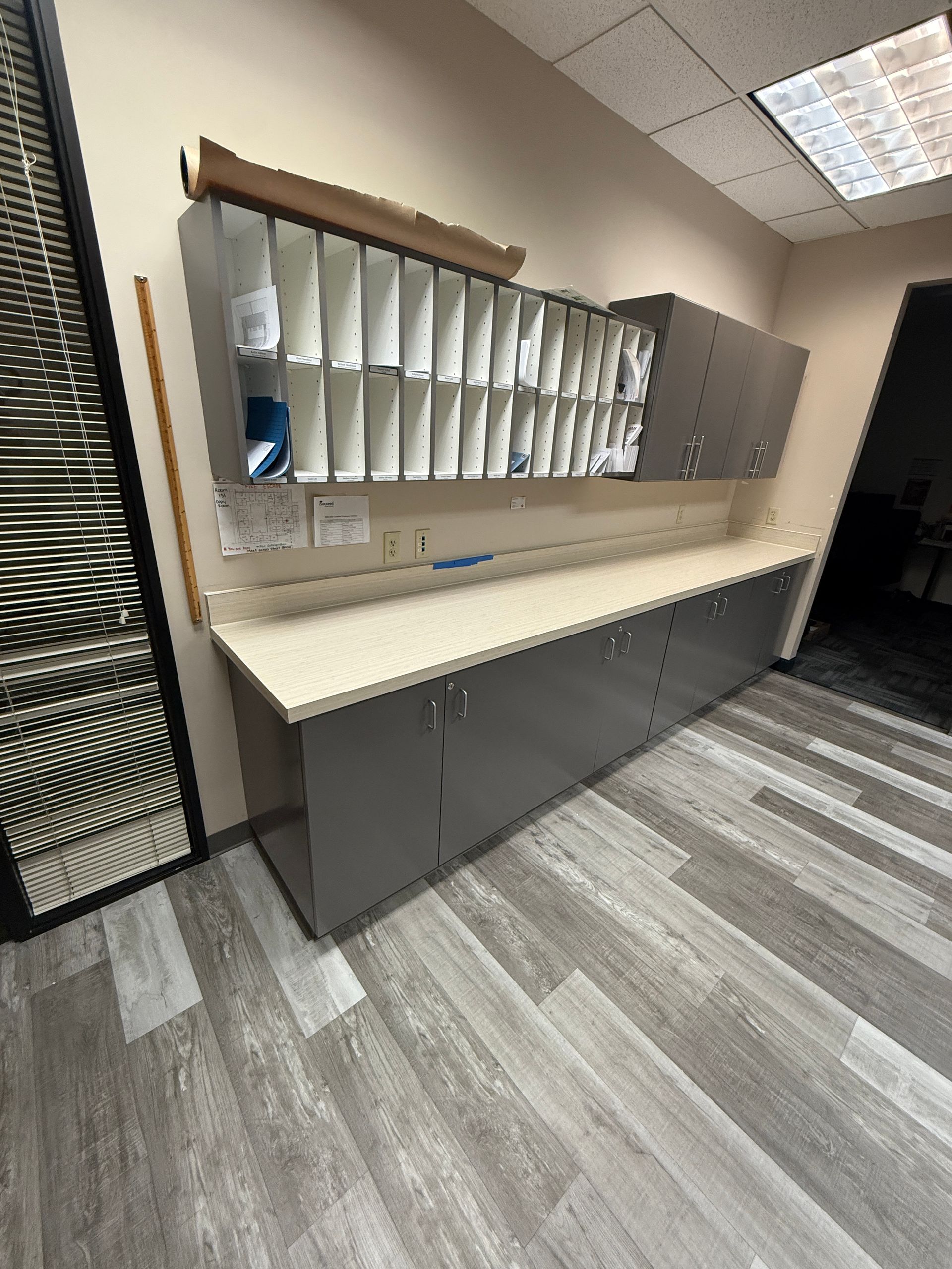 Office wall with mail slots and beige countertop beneath fluorescent ceiling lights.