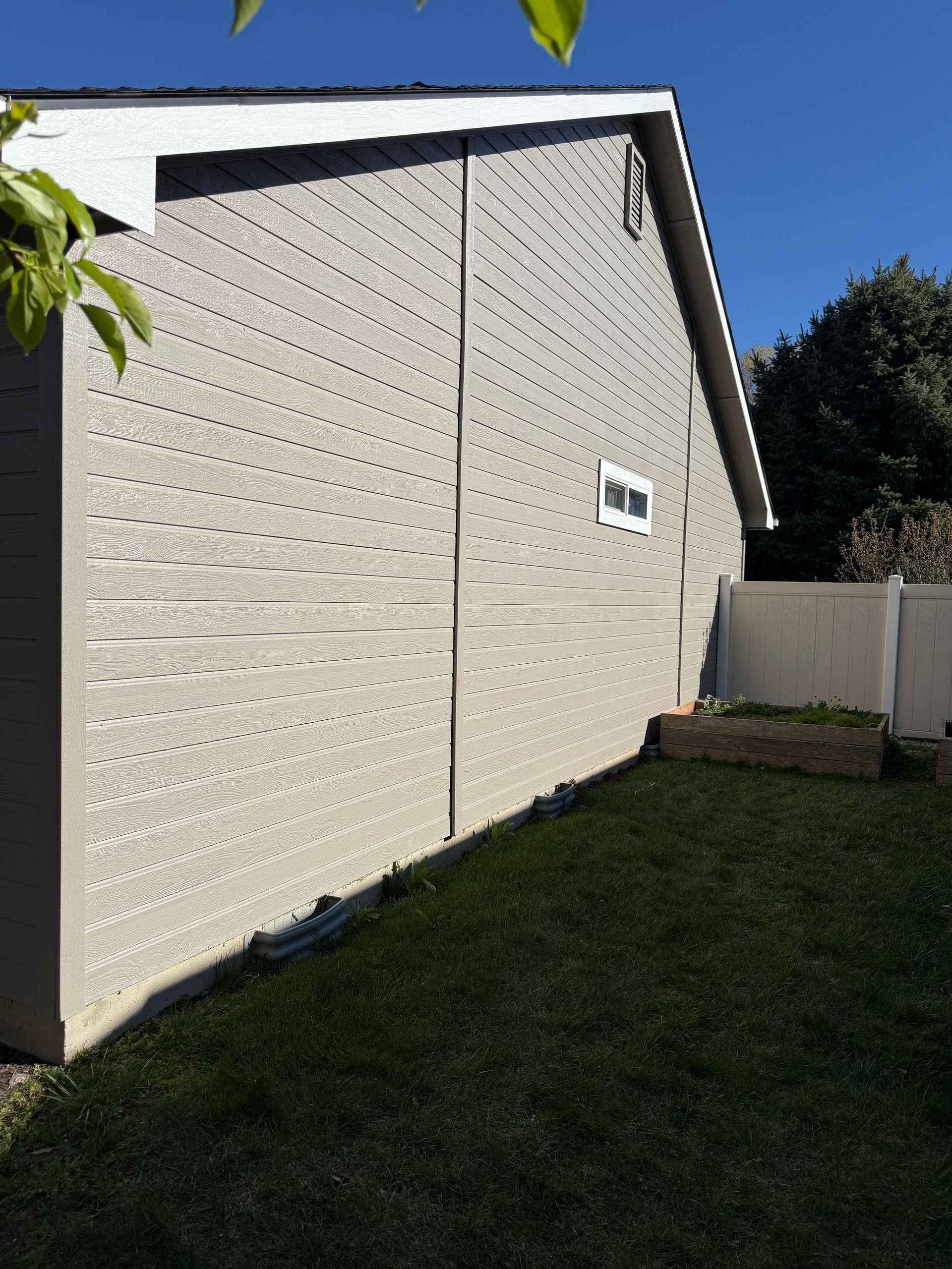 White textured shed wall beside a grassy yard under a blue sky, with a fence at right.