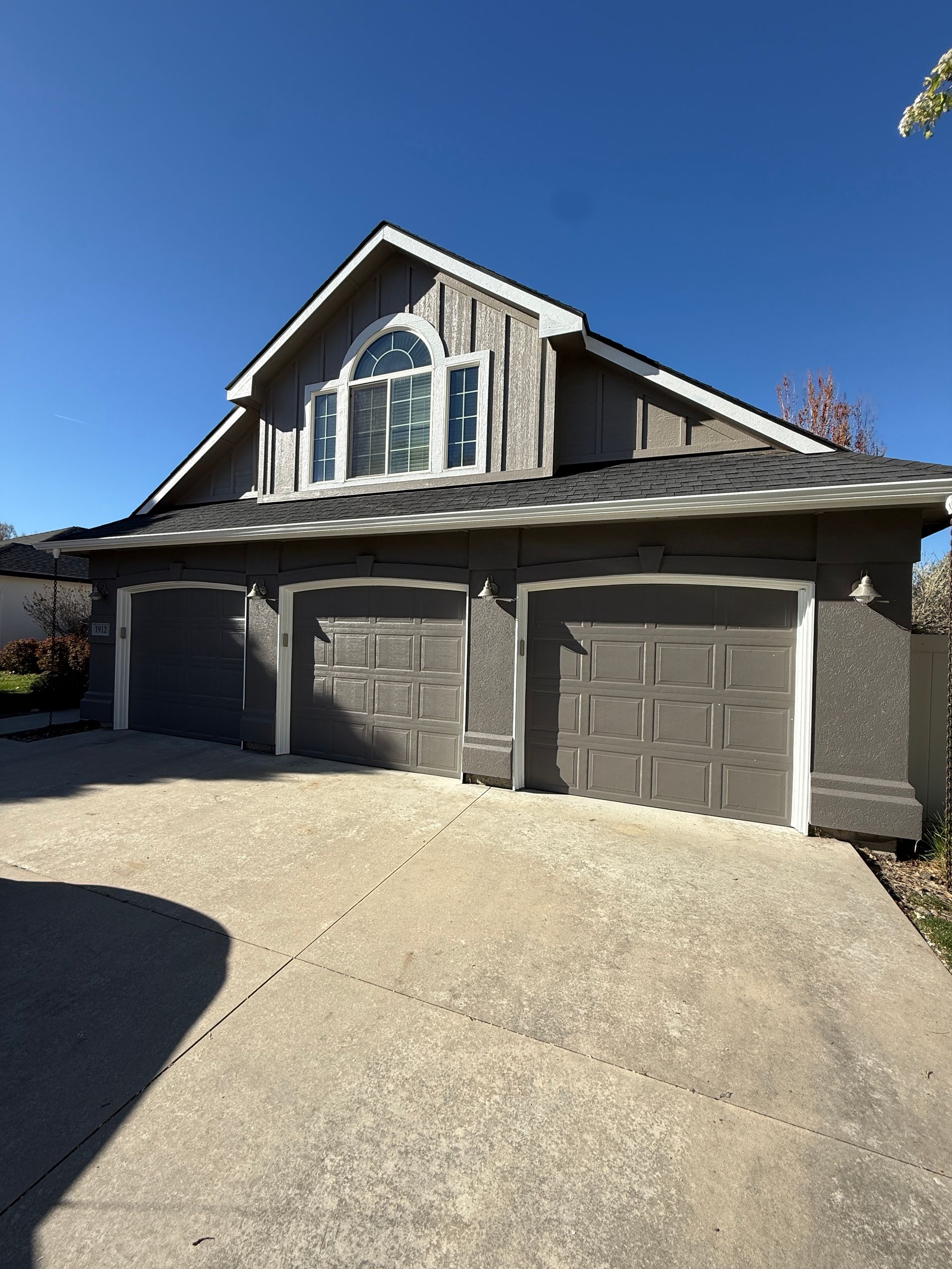 Three-car garage with gray doors and a peaked roof under a clear blue sky