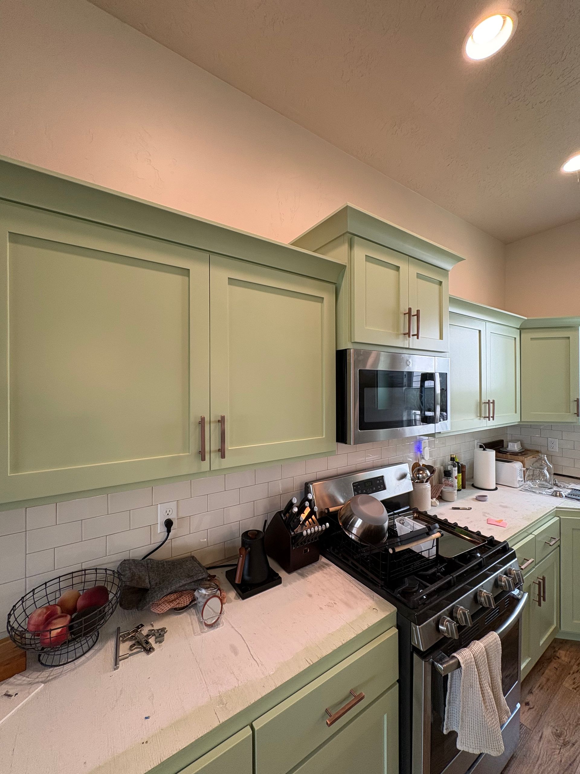 Modern kitchen with mint cabinets, granite counters, stove, microwave, and sink under warm ceiling lights