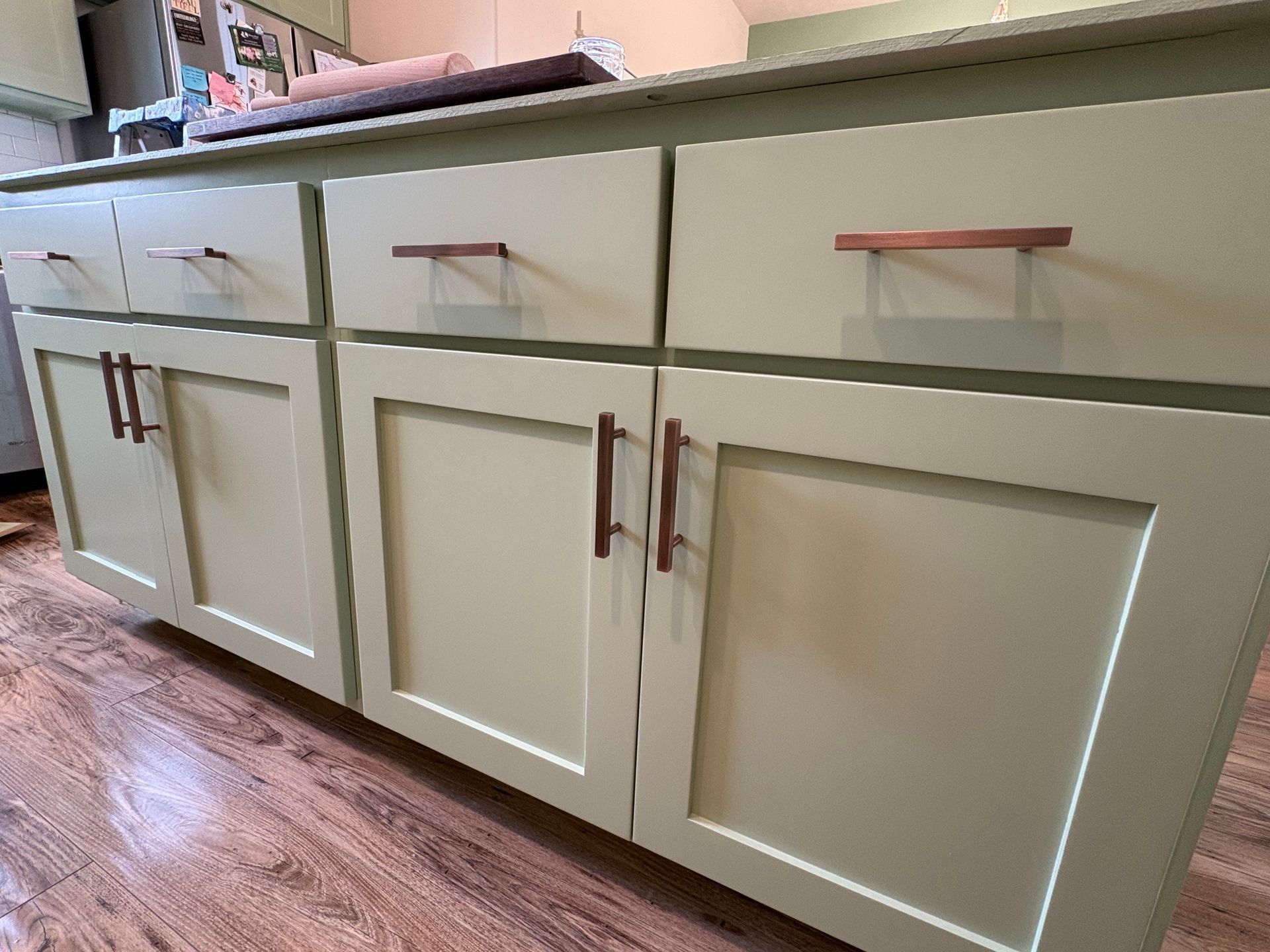 Kitchen cabinets painted pale green with wood handles and a light wood countertop.