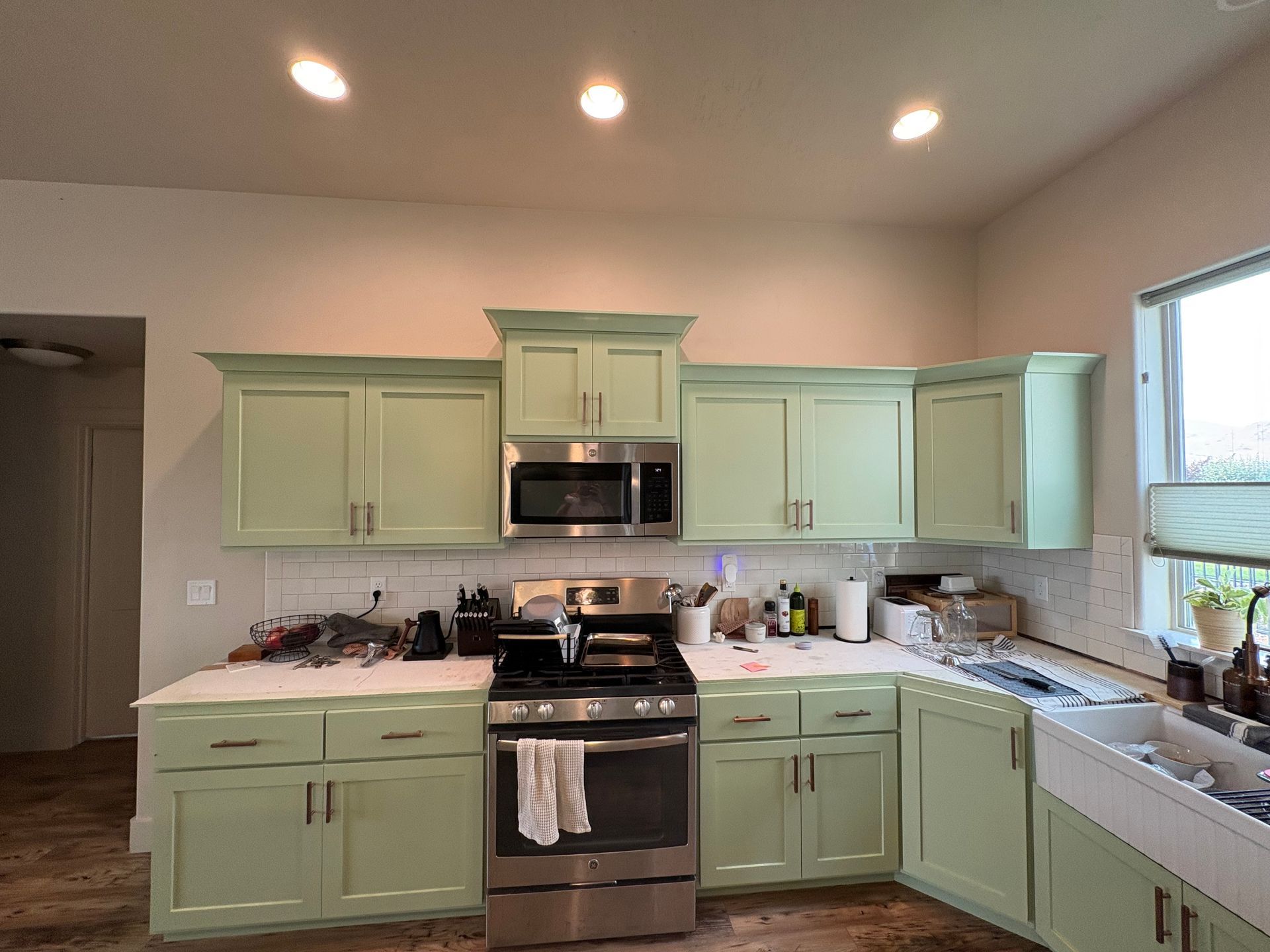 Mint green kitchen with stove, microwave, sink, and countertops under bright ceiling lights