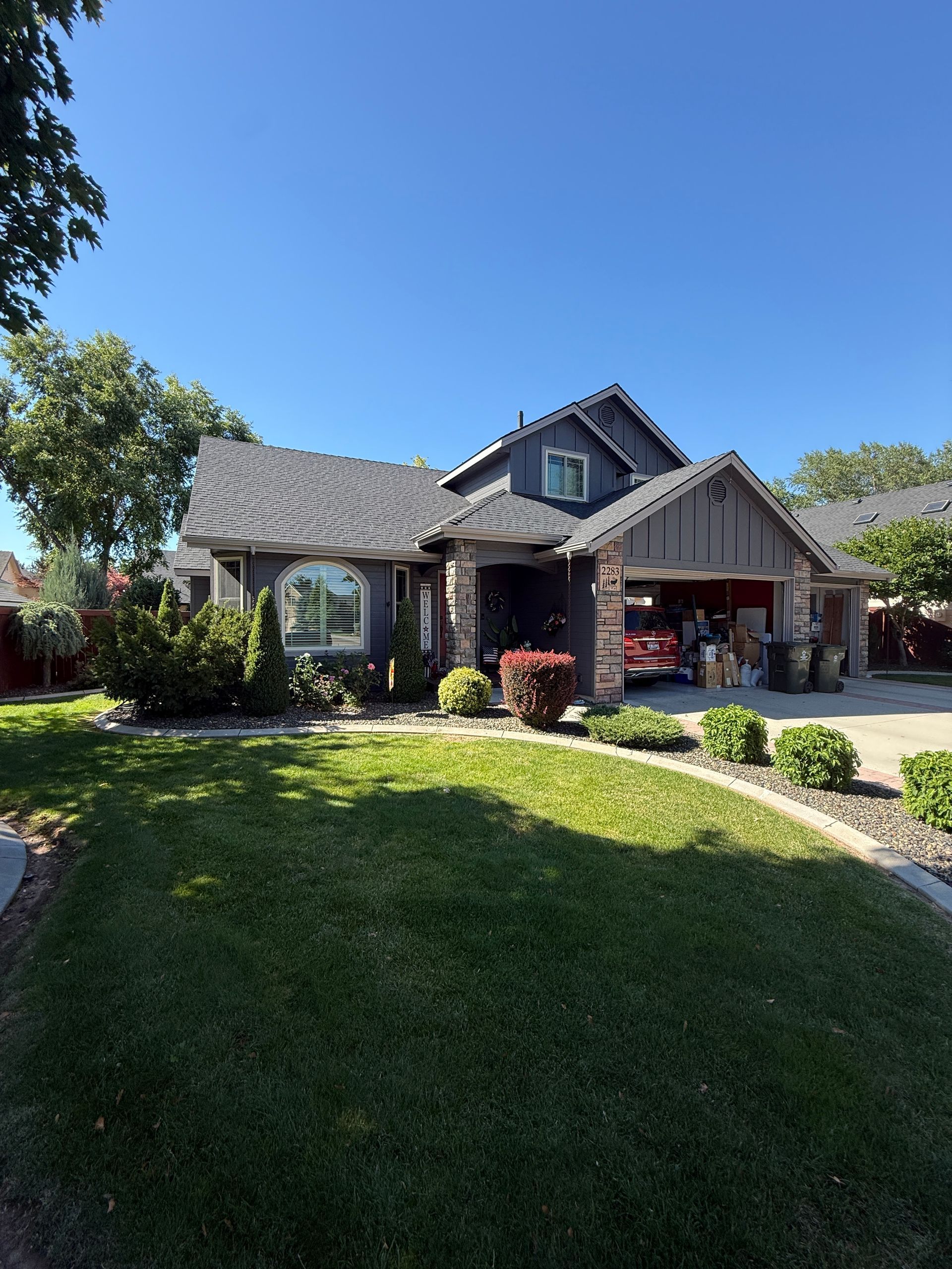 Suburban house with stone facade, front porch, and a sunlit green lawn under a blue sky