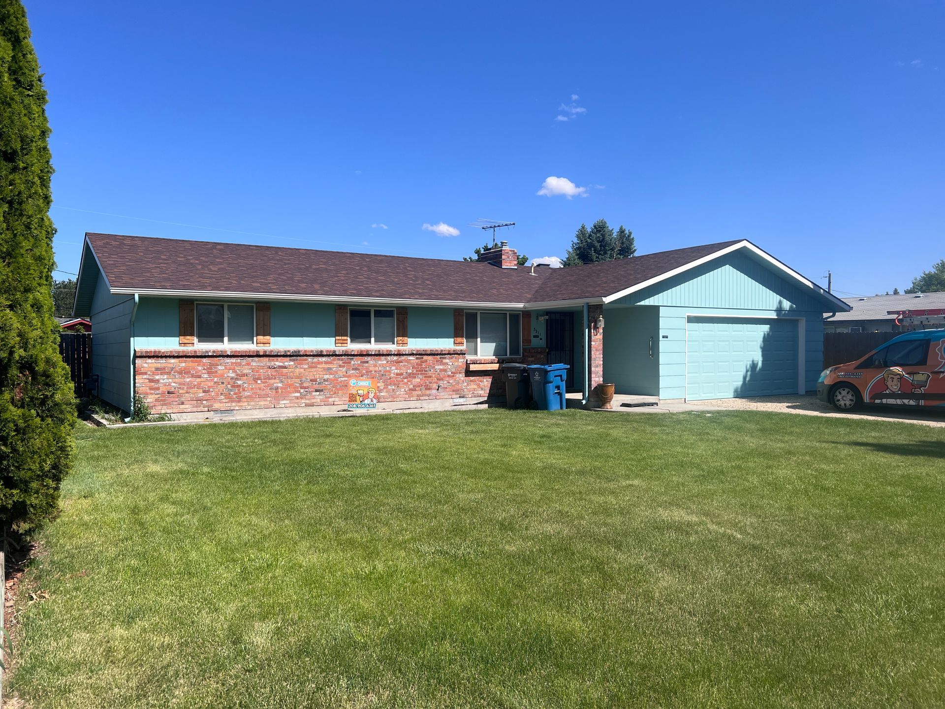 Single-story brick-and-blue house with a green lawn and clear blue sky