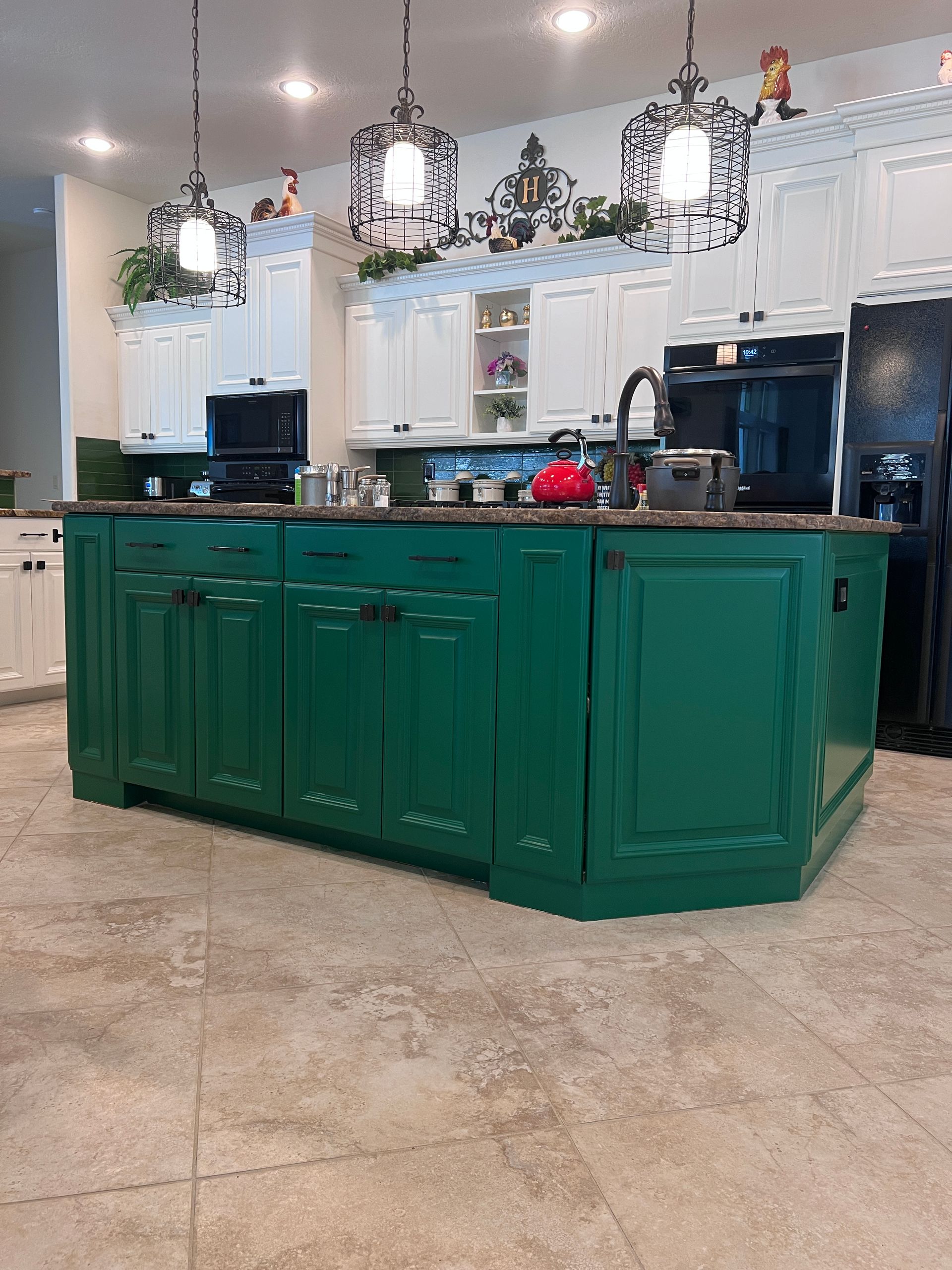 Bright kitchen with a large green island, white cabinets, and hanging pendant lights