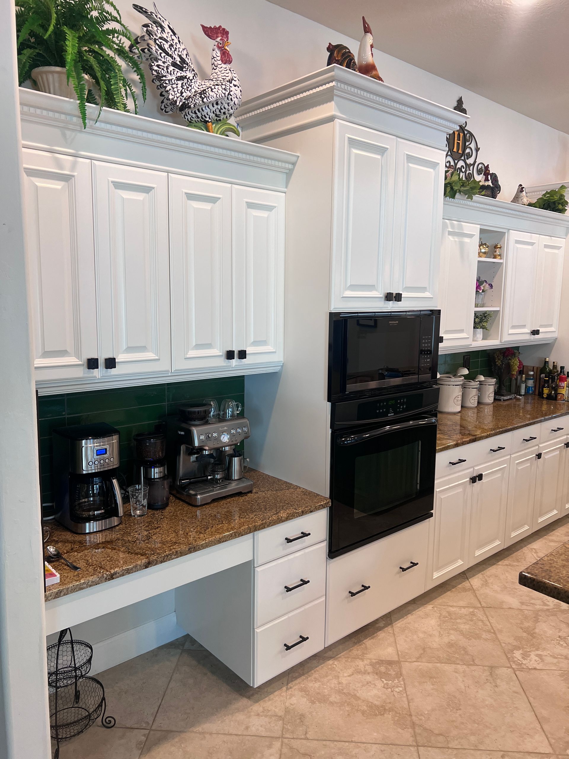 Long white kitchen cabinets with granite counters, built-in oven, and decorative plants on top