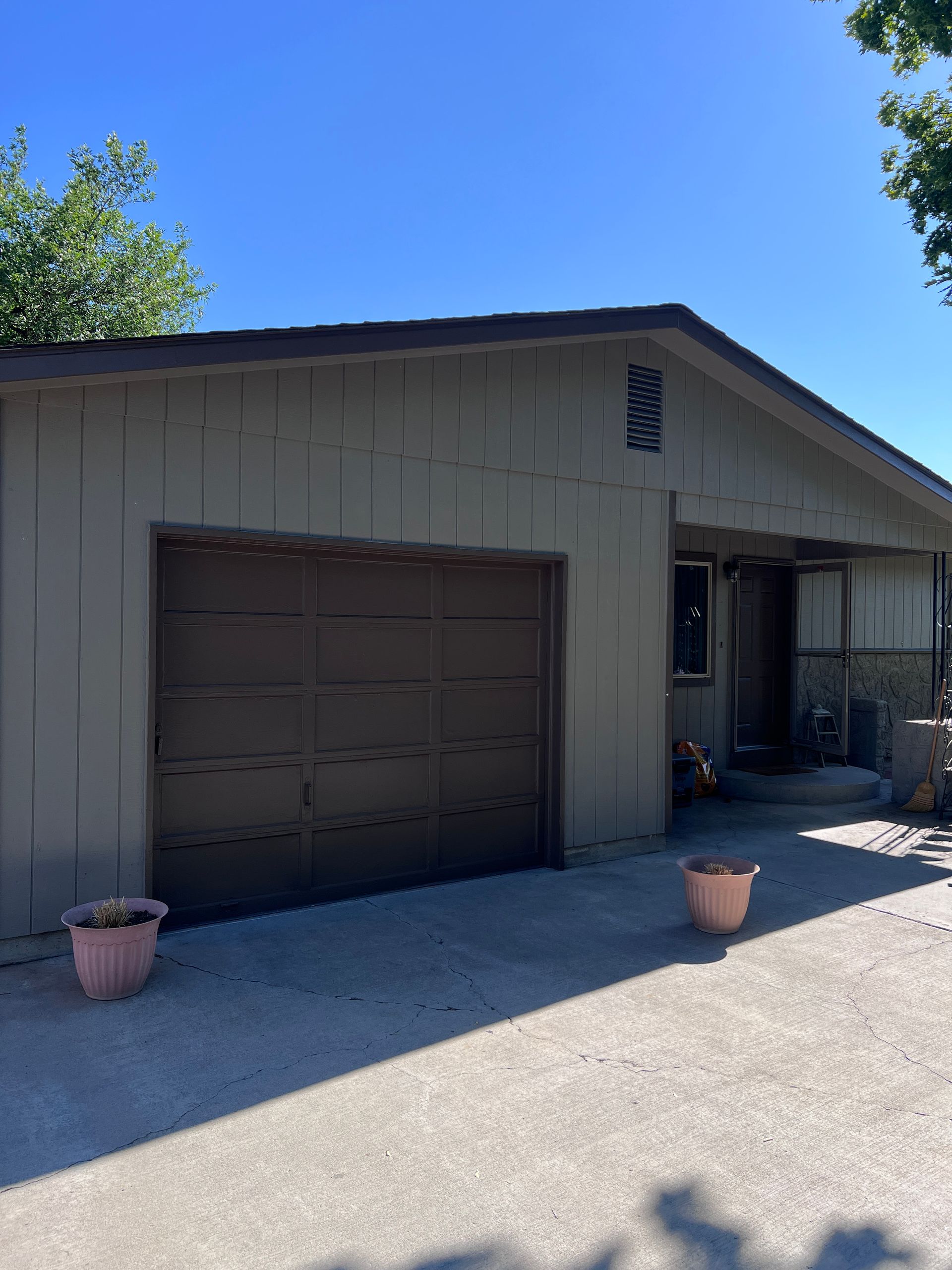 Single-story tan house with a garage, front porch, and potted plants under a clear blue sky