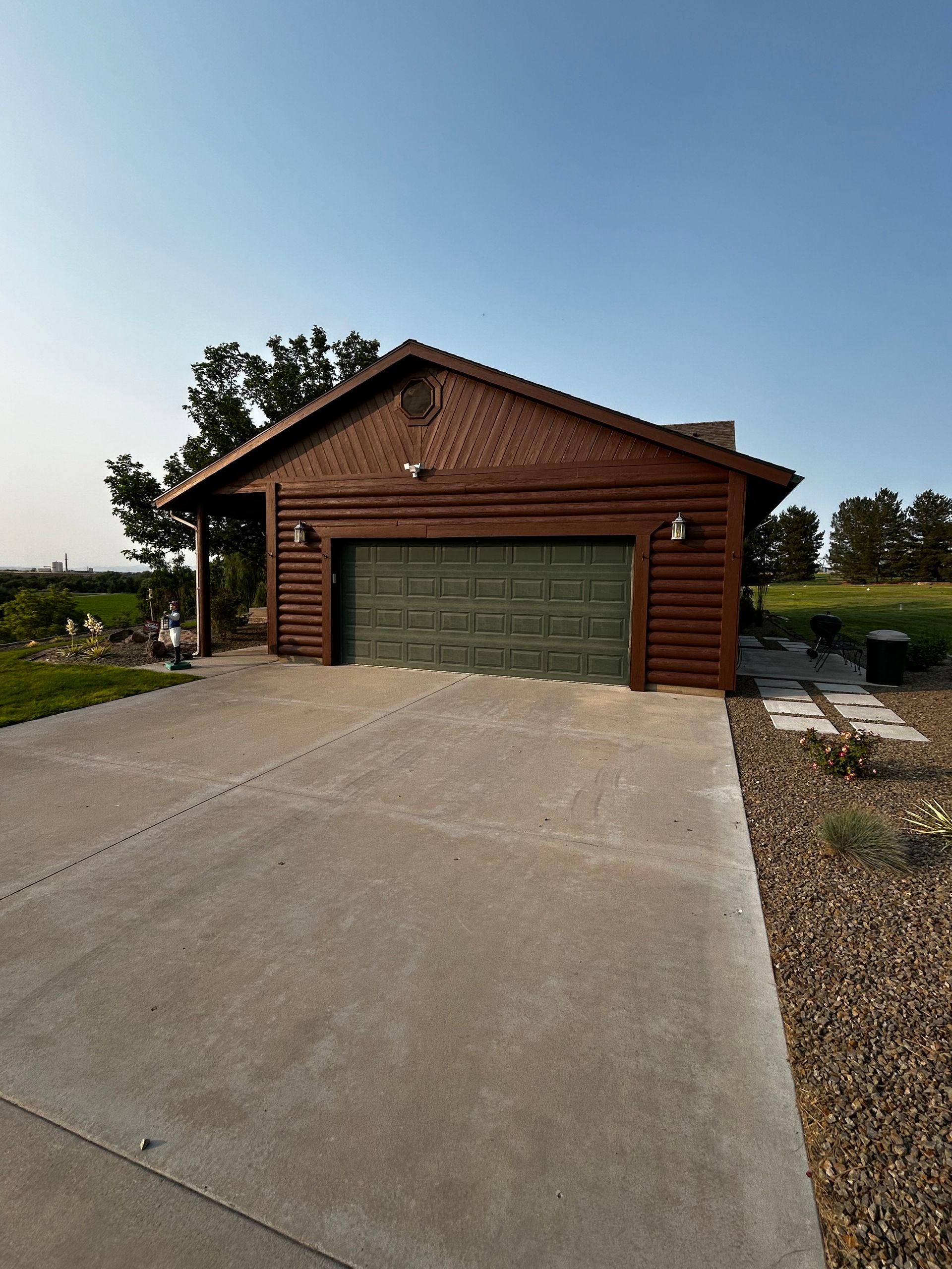 Rustic wooden garage with green doors at the end of a concrete driveway under a clear blue sky