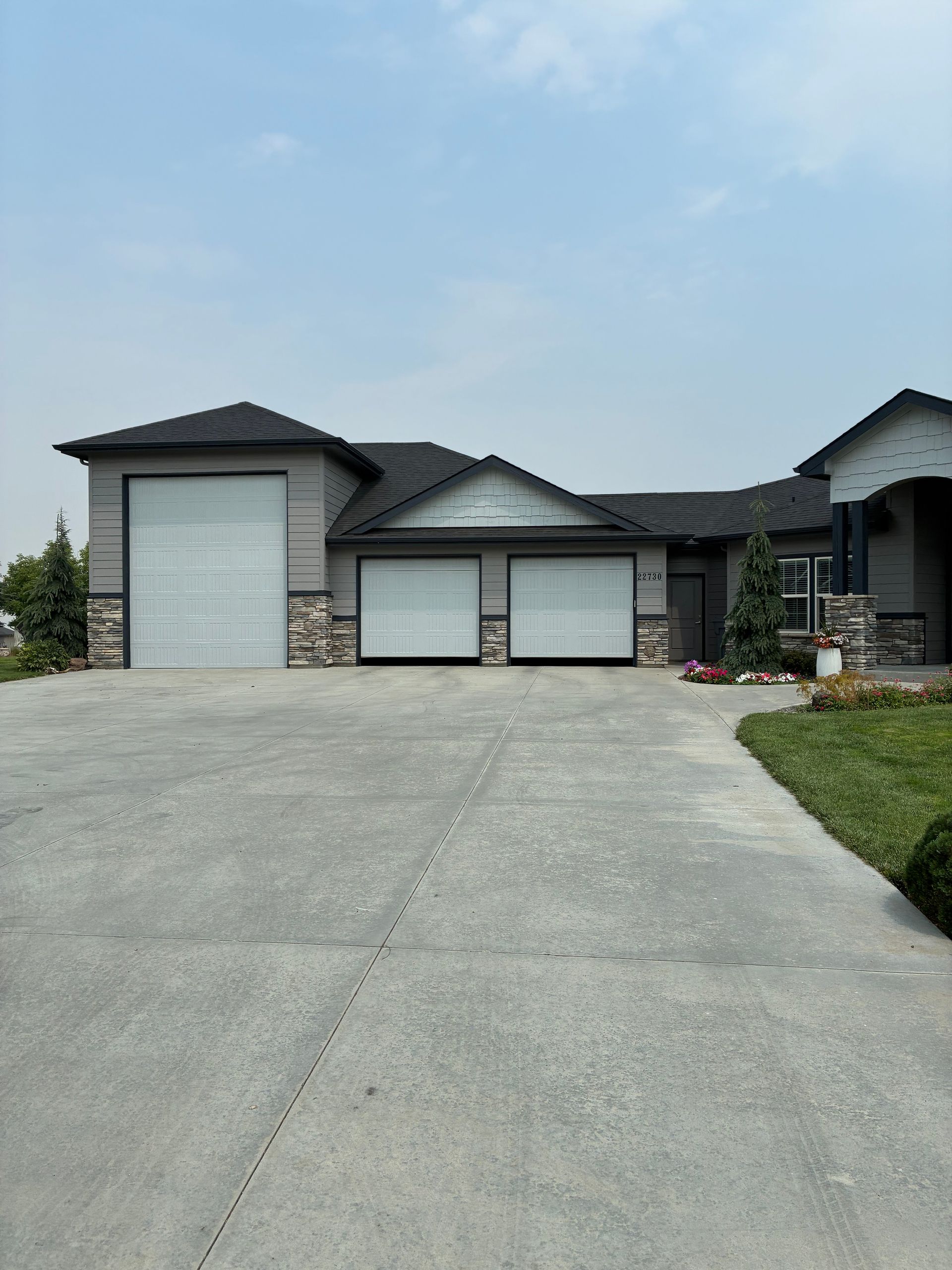 Modern house with three-car garage and a wide concrete driveway under a partly cloudy sky