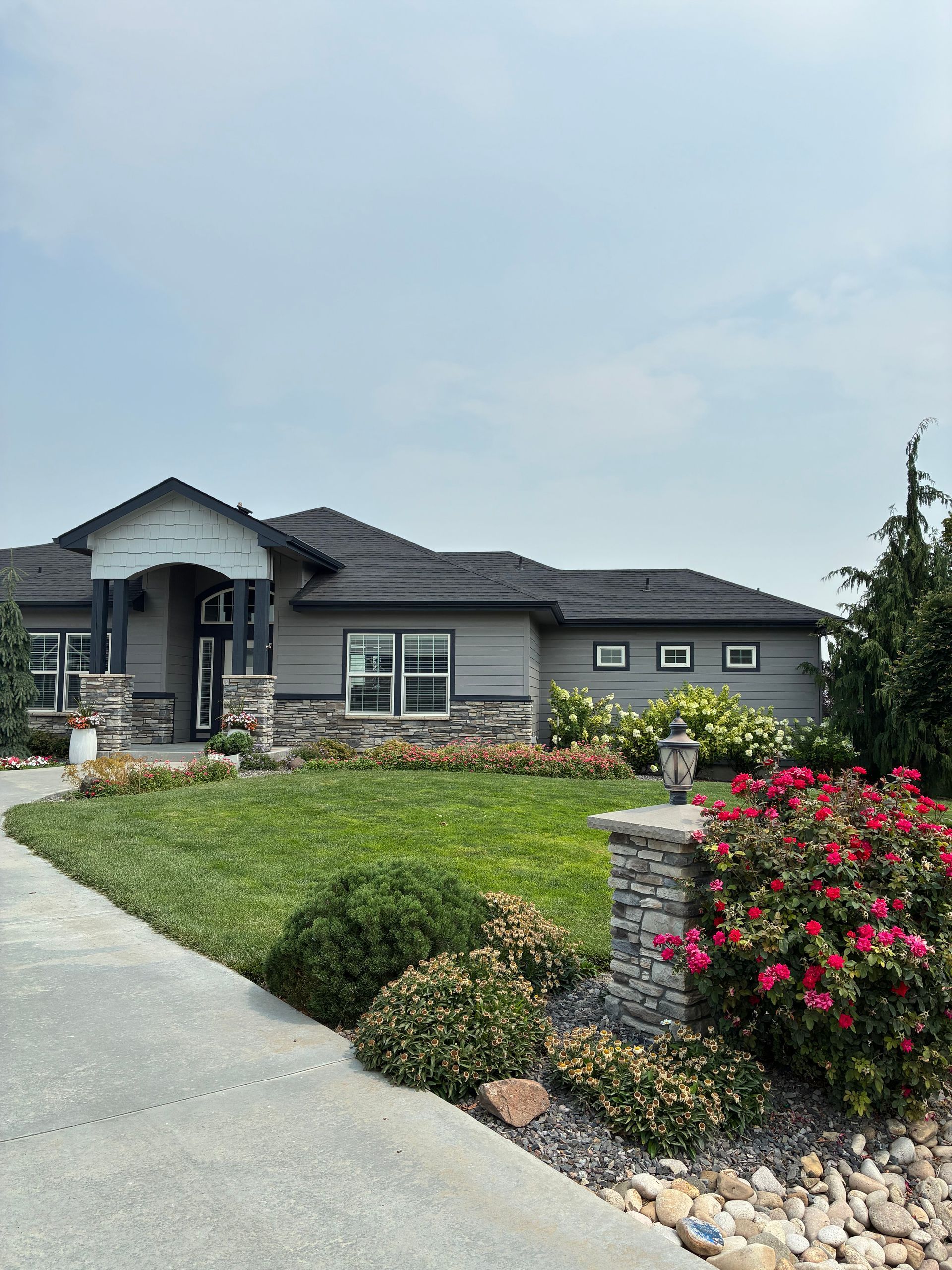 Suburban house with gray siding, manicured lawn, flower beds, and a concrete driveway under a cloudy sky