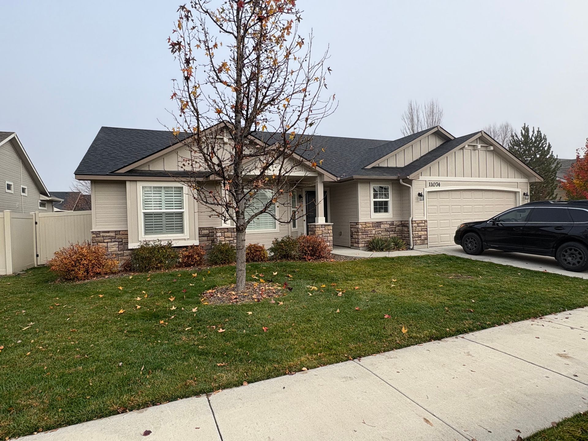 Single-story suburban house with a front lawn, leafless tree, and a black car in the driveway
