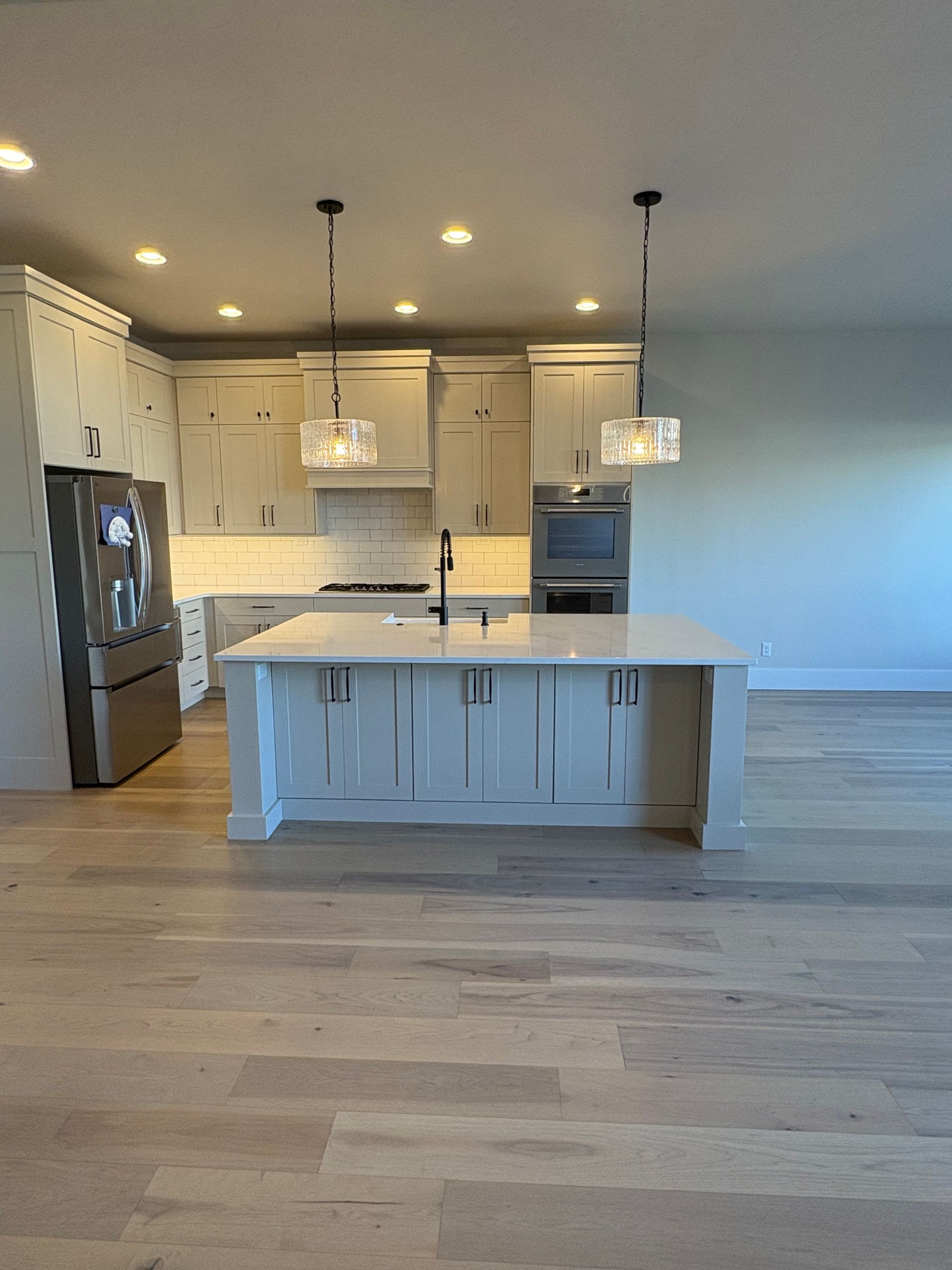 Modern white kitchen with island, pendant lights, stainless fridge, and light wood floors