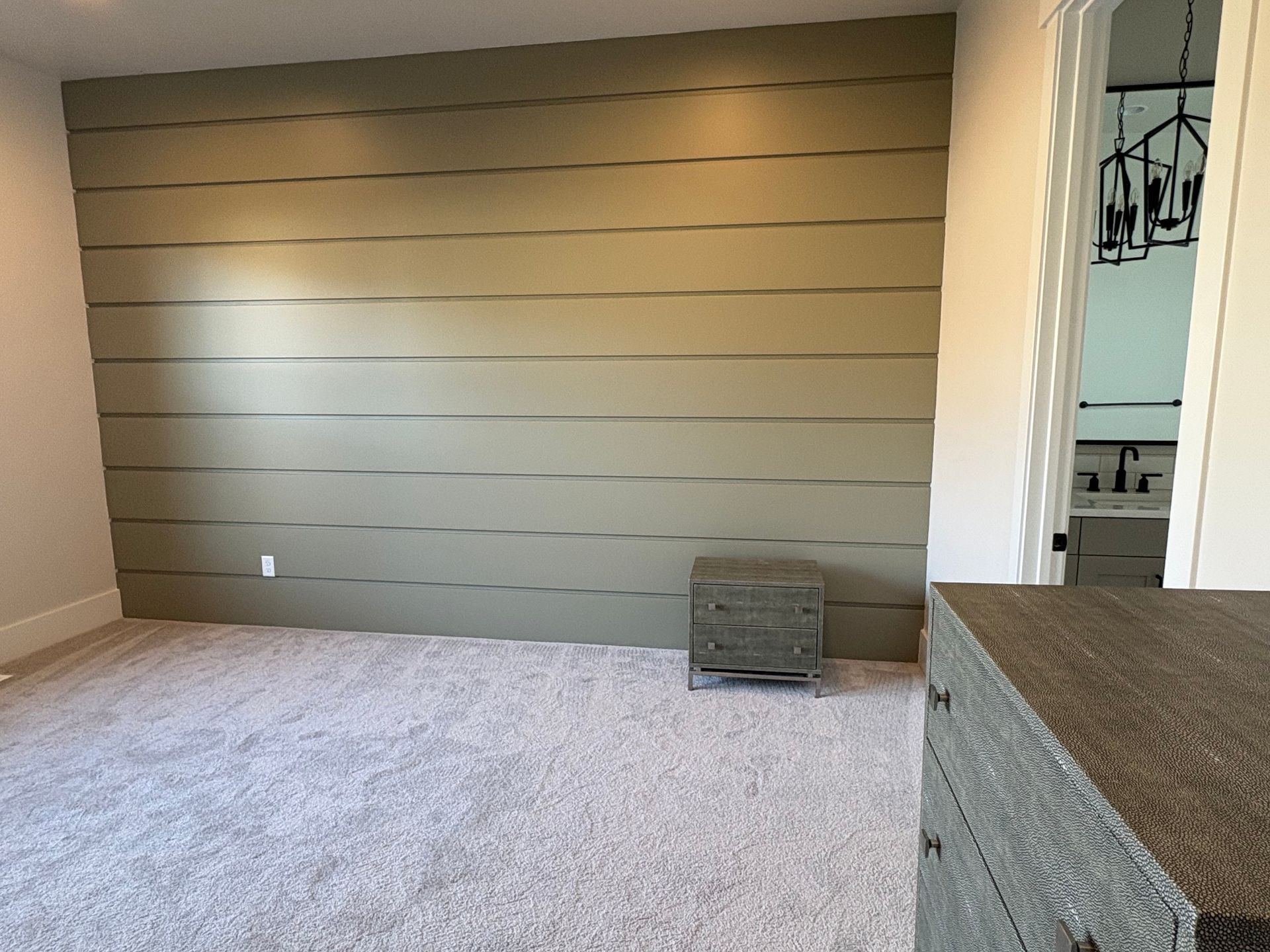 Empty carpeted room with a tan shiplap accent wall and a small gray ottoman