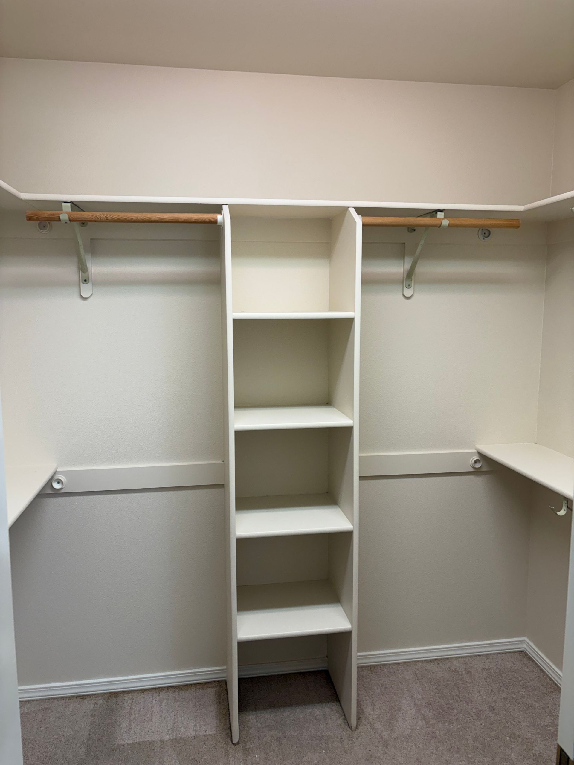 Empty walk-in closet with white shelves, hanging rods, and carpeted floor