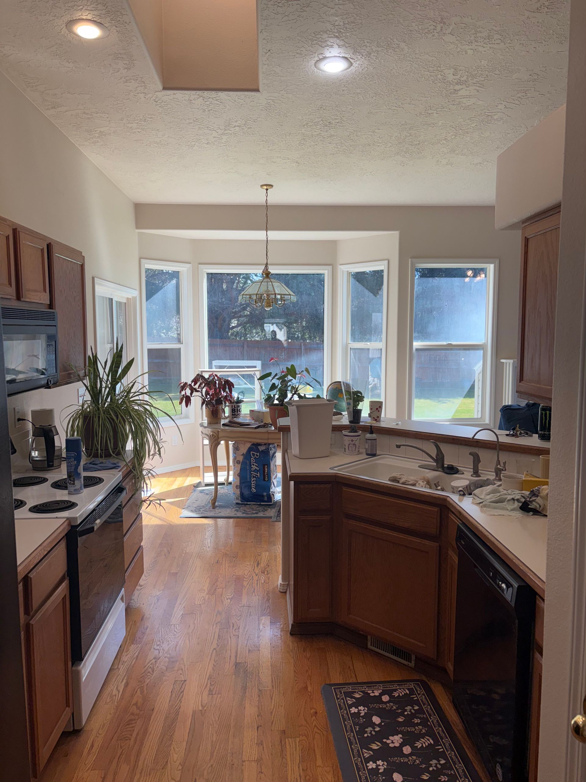 Bright kitchen with wooden cabinets, island sink, and large windows overlooking trees.