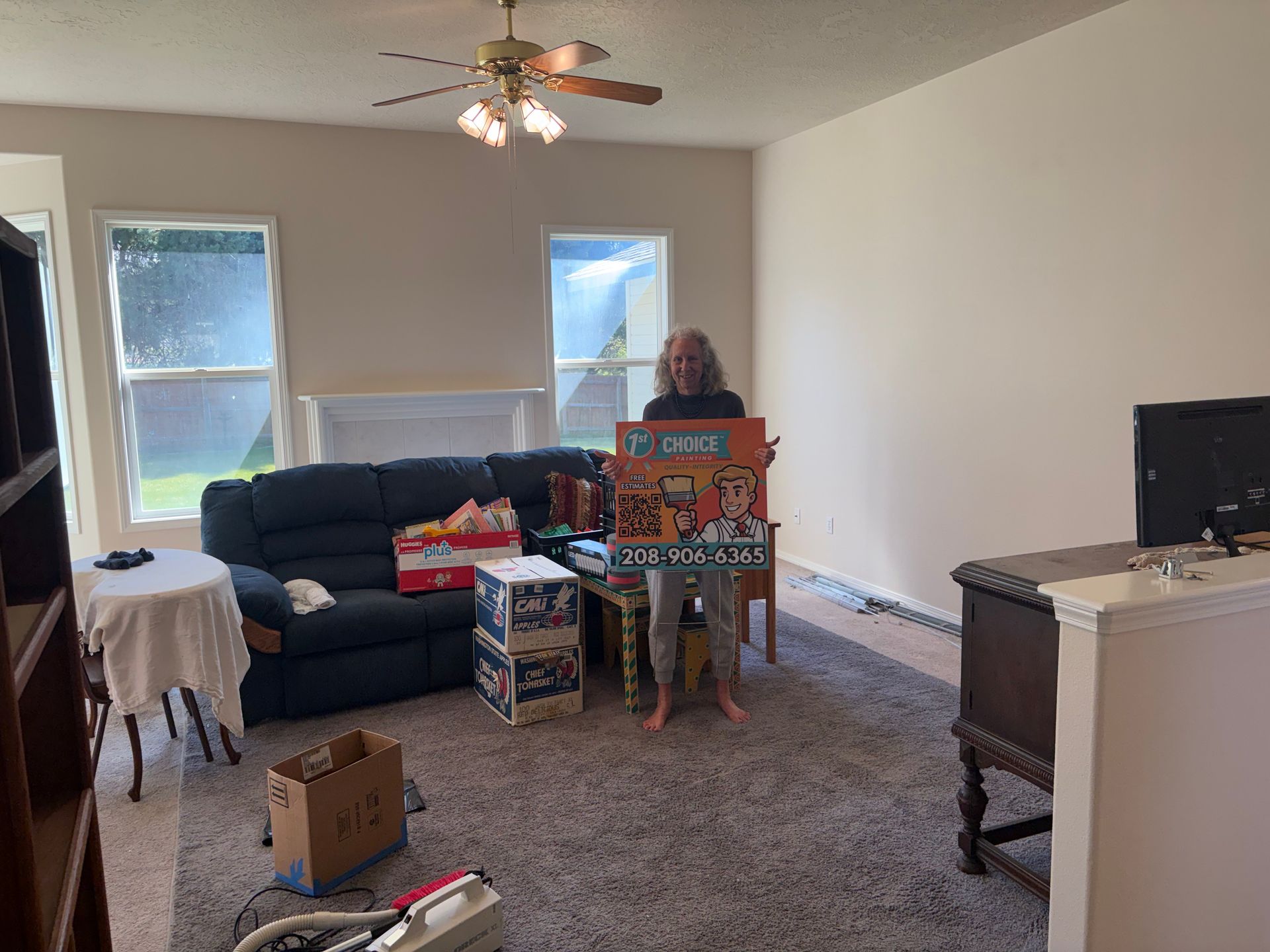 Living room with boxes and a person standing by stacked board games near a sofa and TV