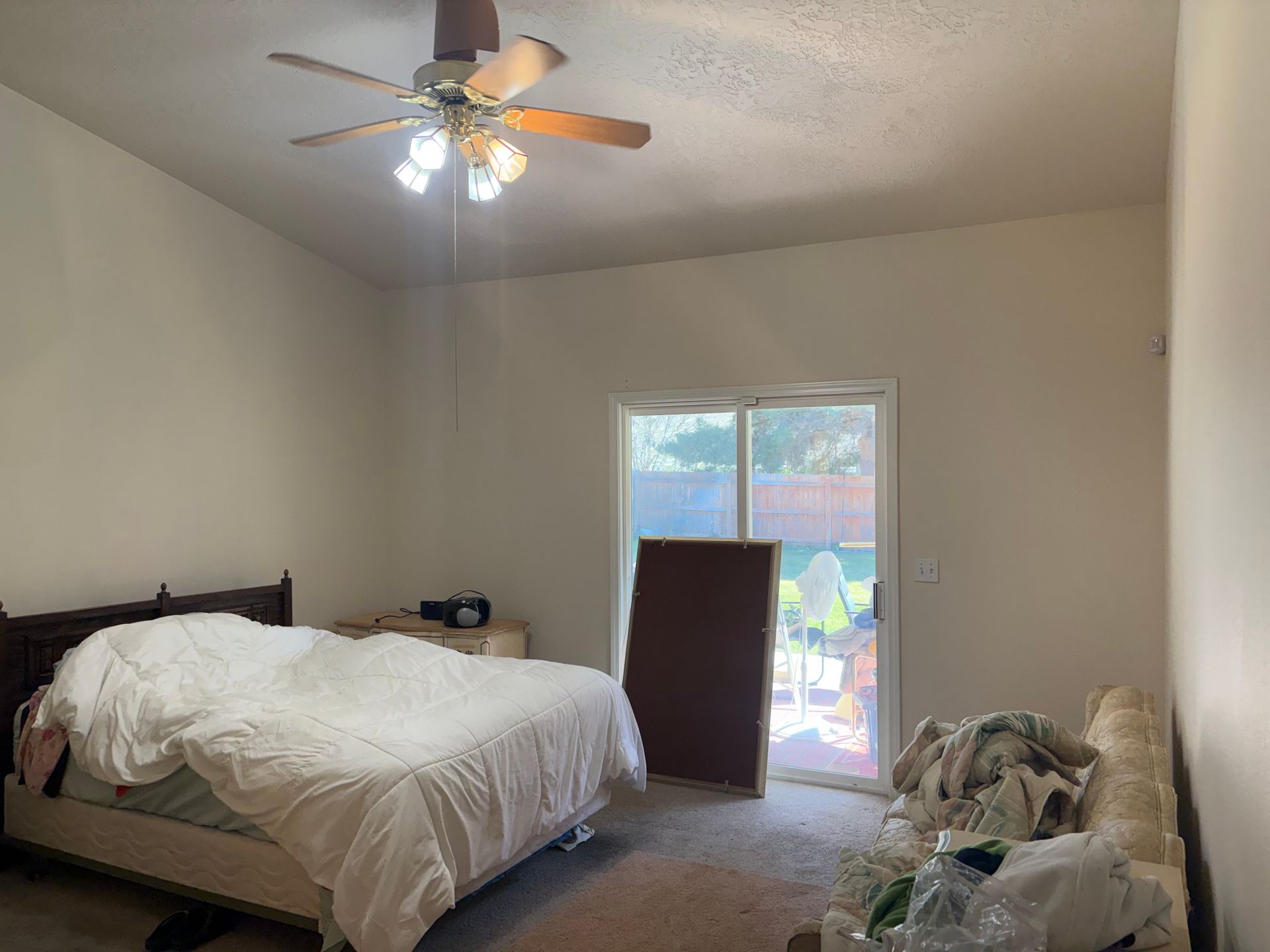 Bedroom with unmade bed, ceiling fan light on, and a window letting in daylight.