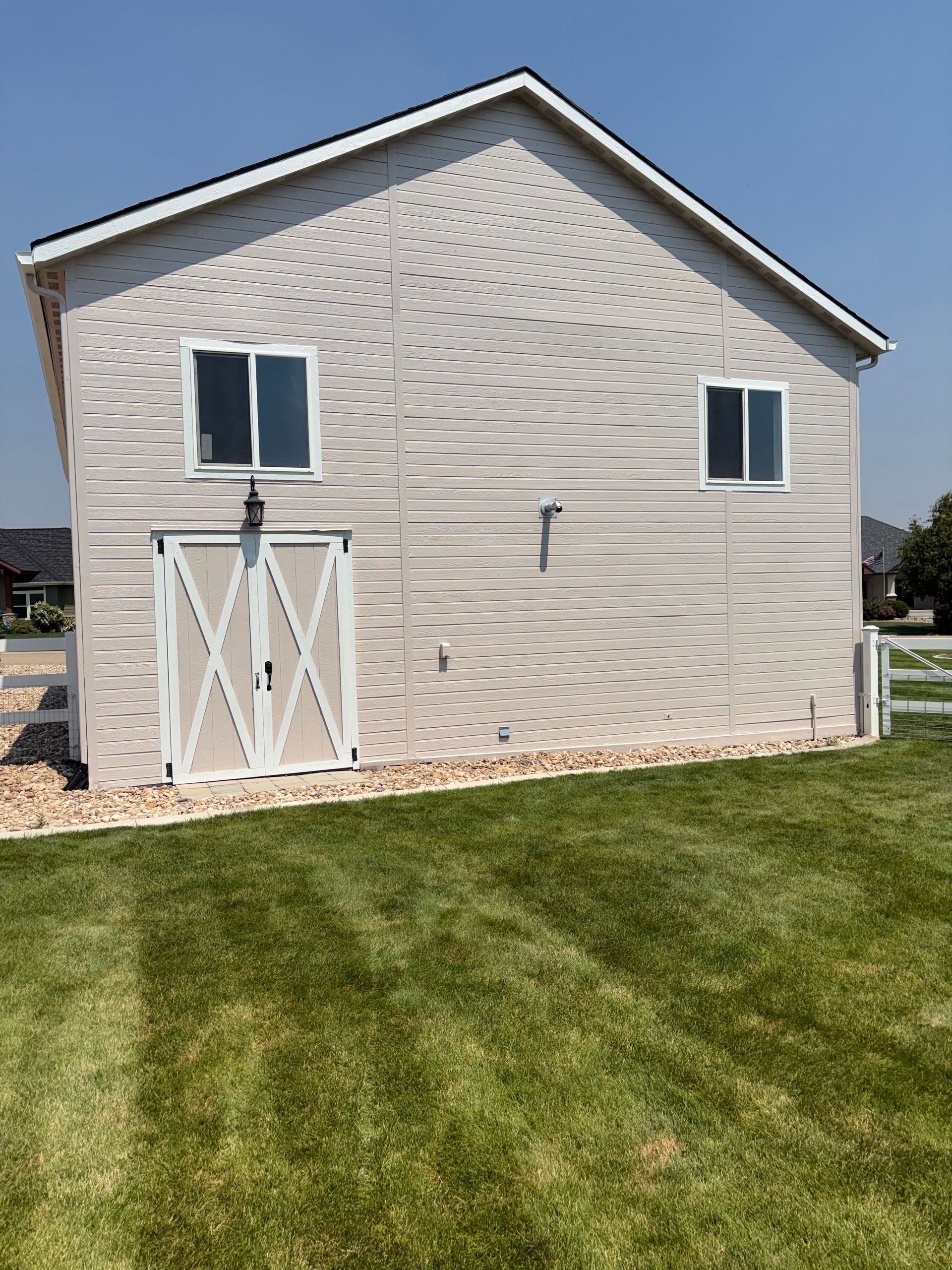 White shed with two windows and double barn doors on a grassy lawn under a blue sky