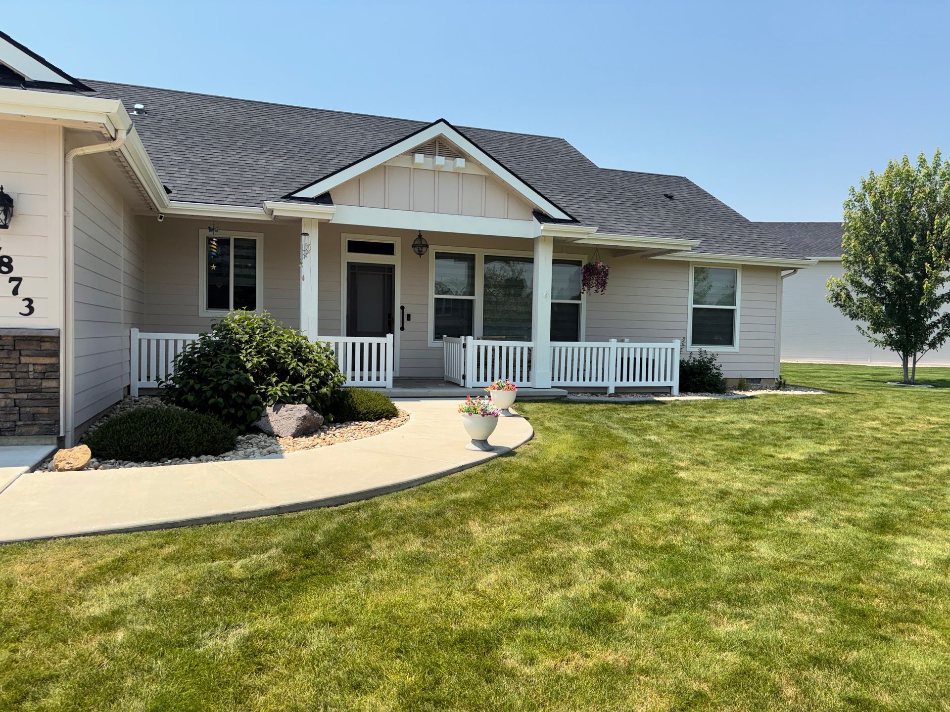 Suburban house with a white porch and curved walkway, front lawn, and clear blue sky