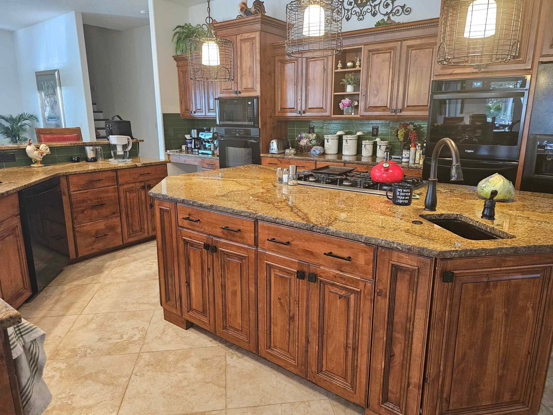Spacious kitchen with wood cabinets, granite island, and black appliances under bright windows.