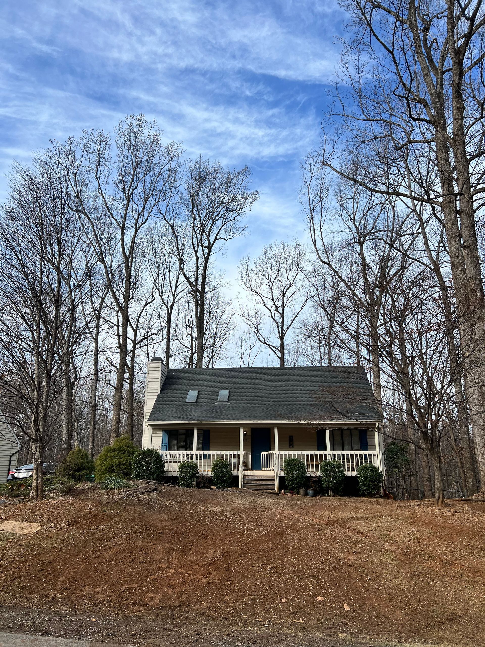 A house with a porch is surrounded by trees on a hill.