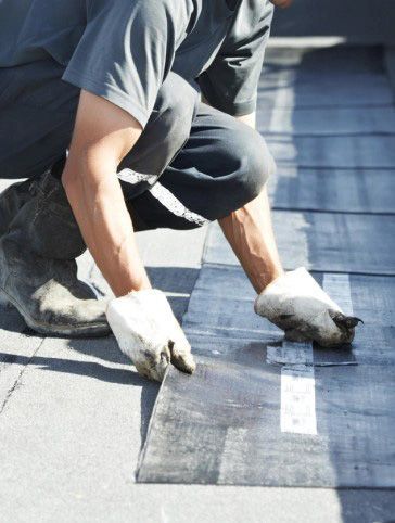 A man is kneeling down and applying a rubber mat to a roof.