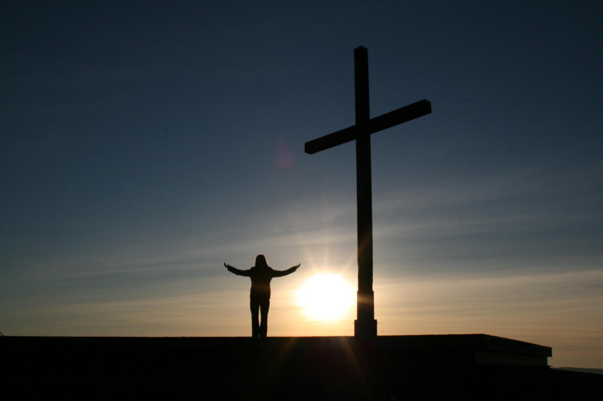 A person standing in front of a cross with their arms outstretched