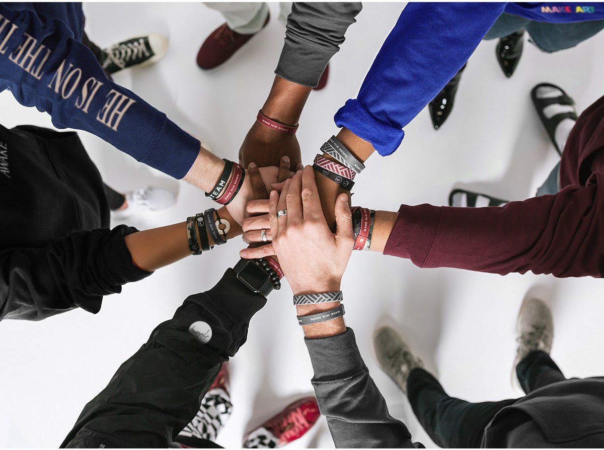 A group of people putting their hands together with one wearing a shirt that says he is on the team