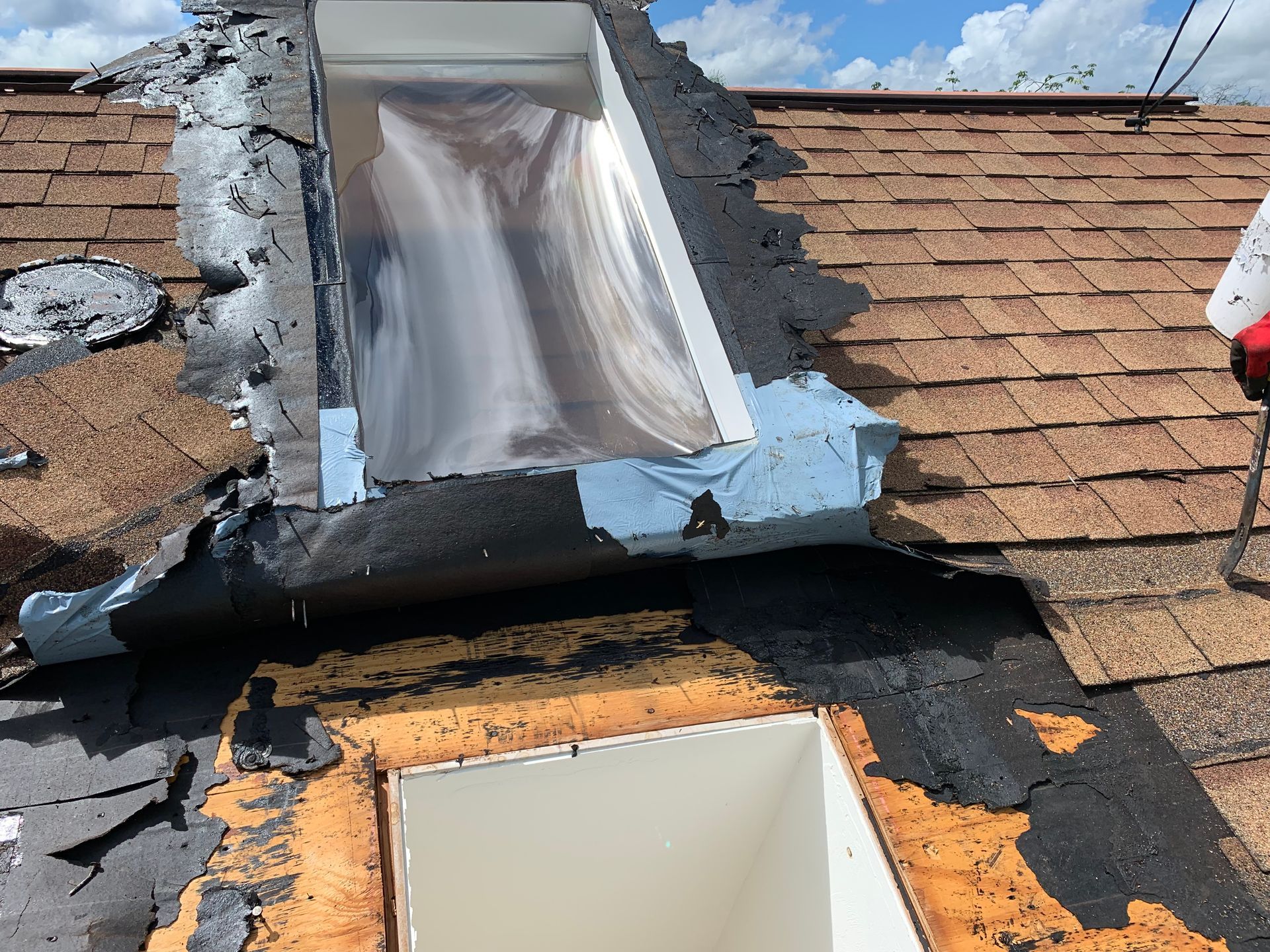 Damaged roof with torn shingles and a broken skylight under repair