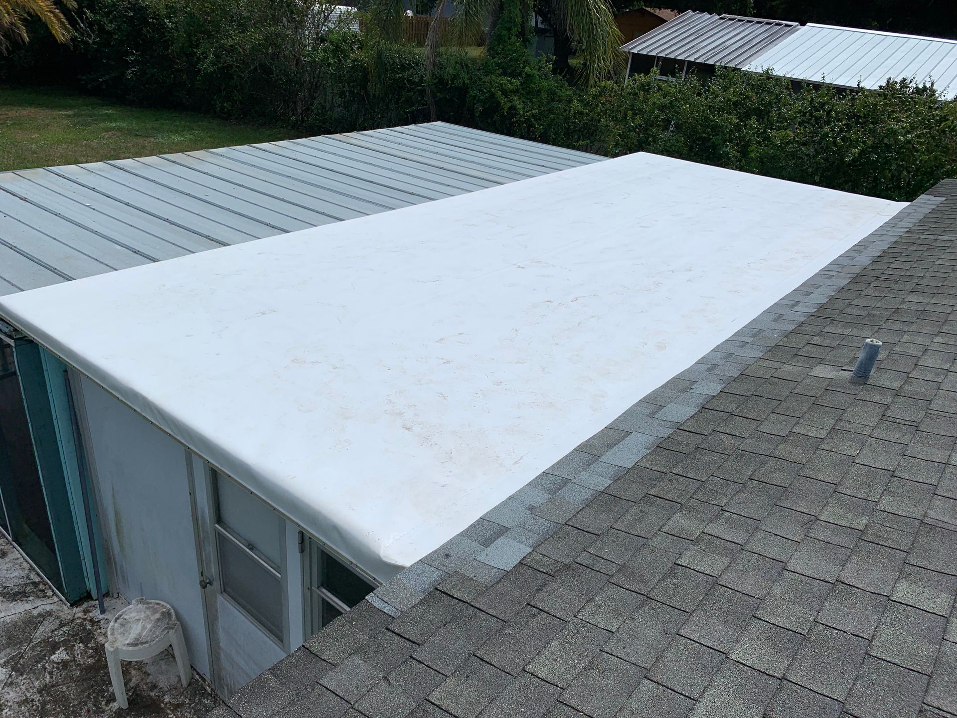 Flat rooftop with a large white tarp covering one section next to gray shingles and solar panels