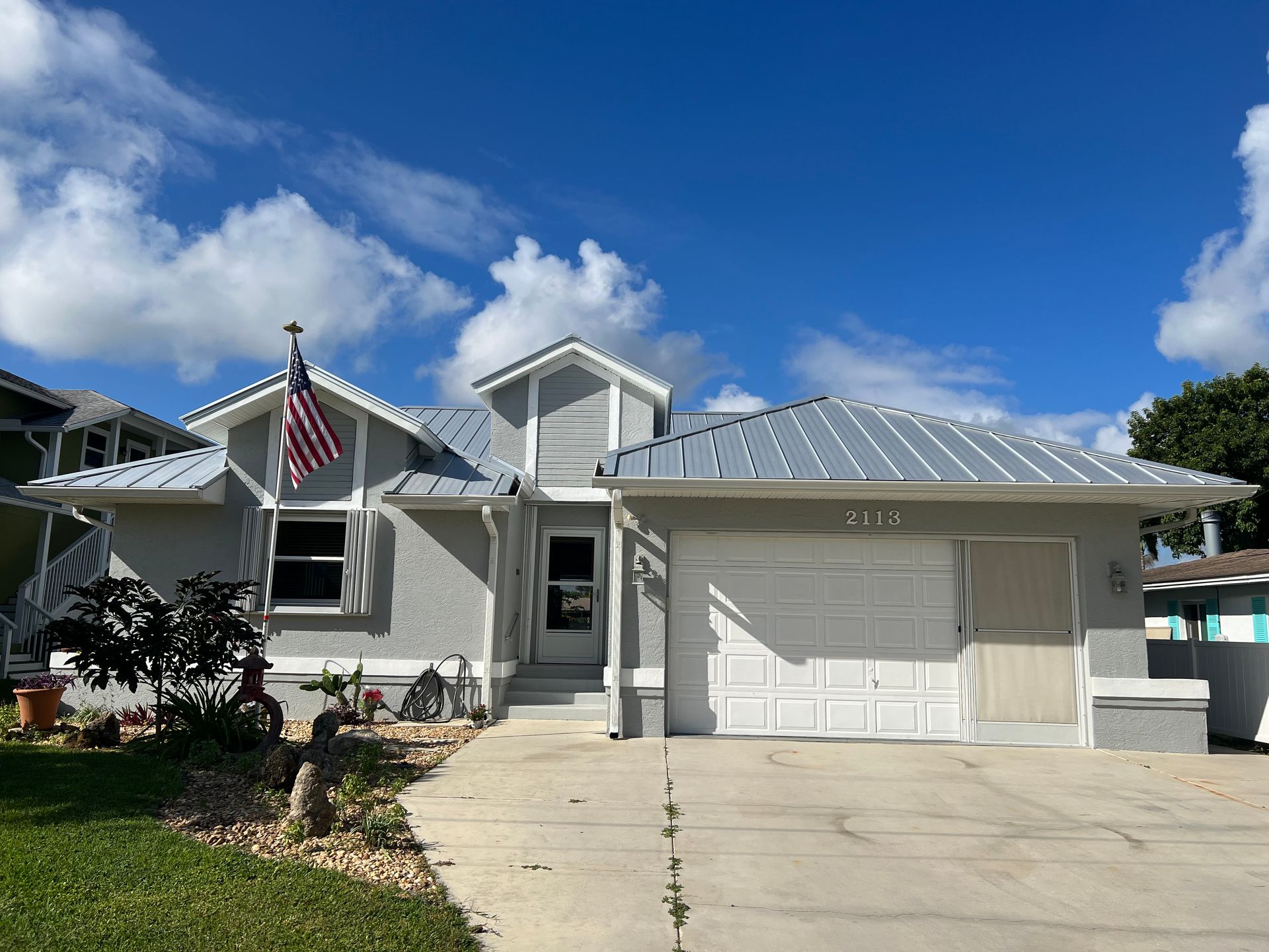 Suburban house with white garage, American flag, and driveway under a clear blue sky