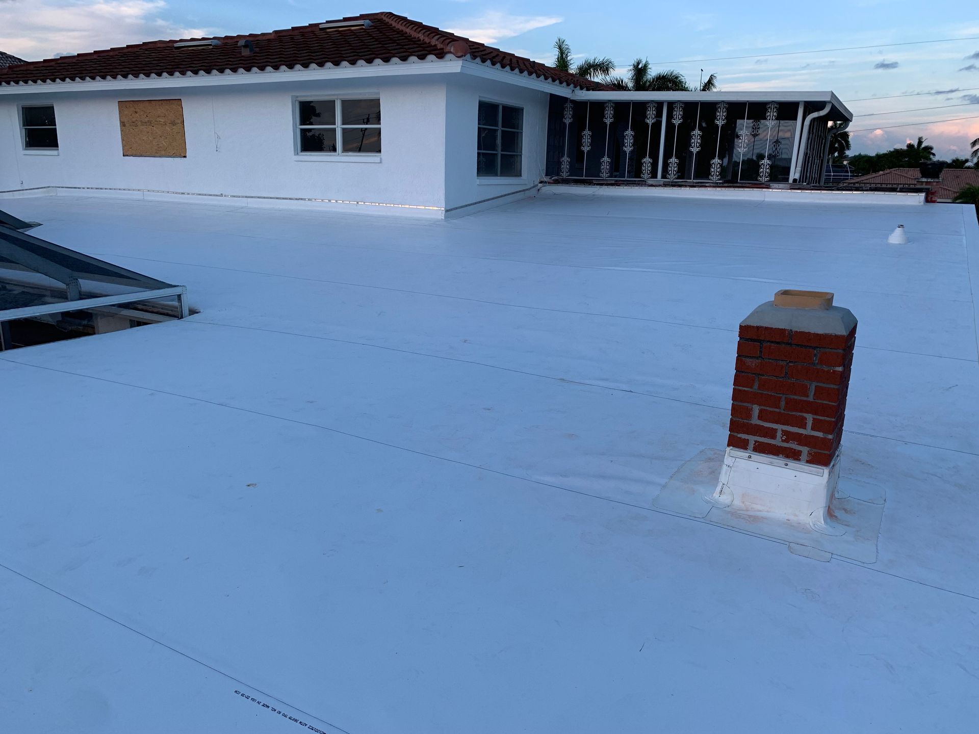 Rooftop patio at dusk with white flooring, a brick vent, and a house with lit windows in the background