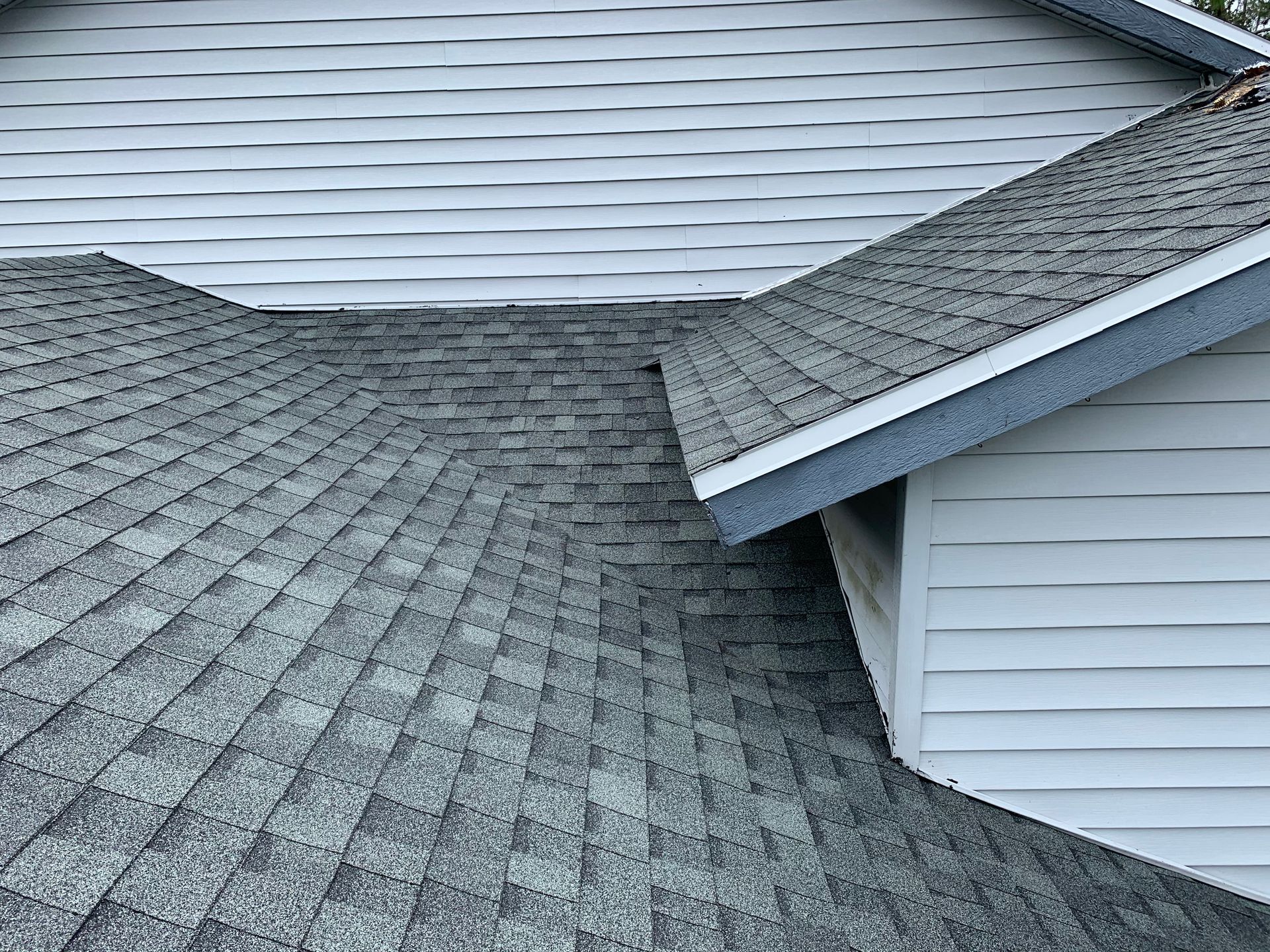 Gray shingled roof with multiple slopes and white siding on a house
