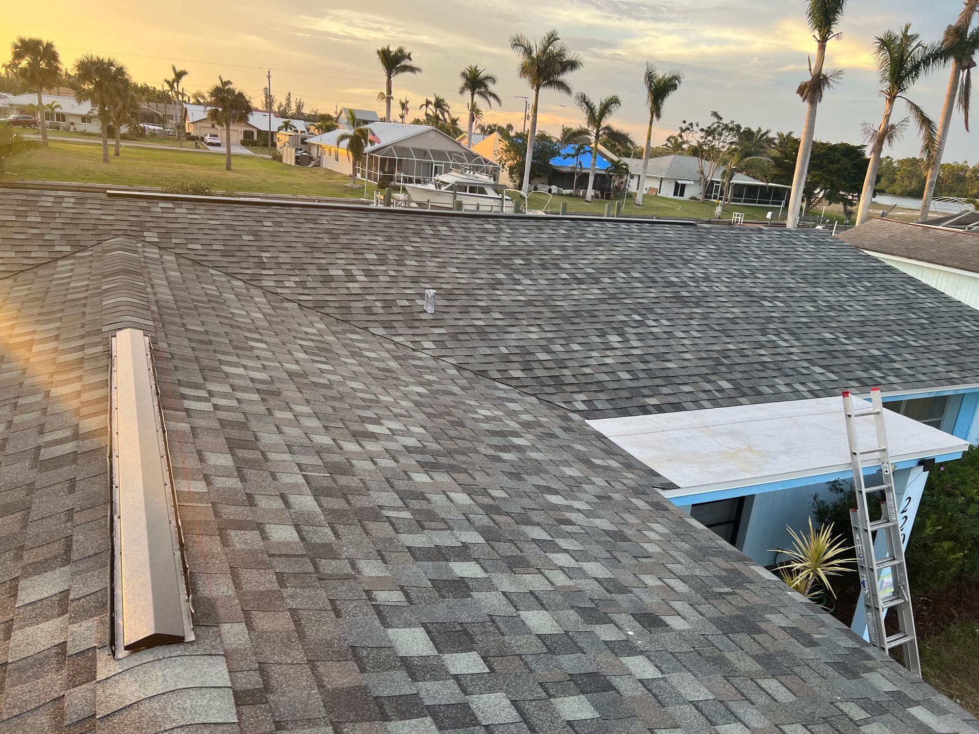 Roof under construction with shingles, rooftop materials, and a coastal neighborhood at sunset