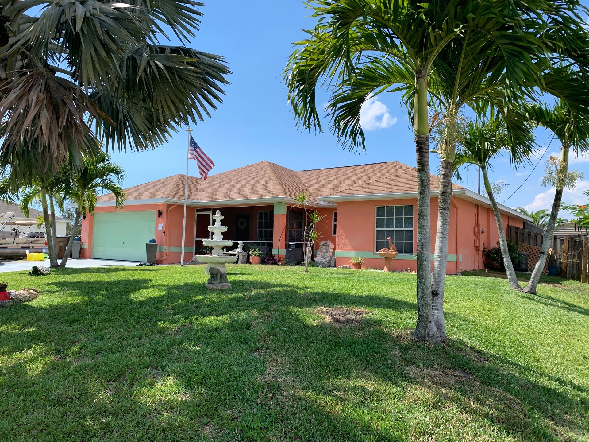 Single-story brick house with red roof, palm trees, and a green lawn on a sunny day