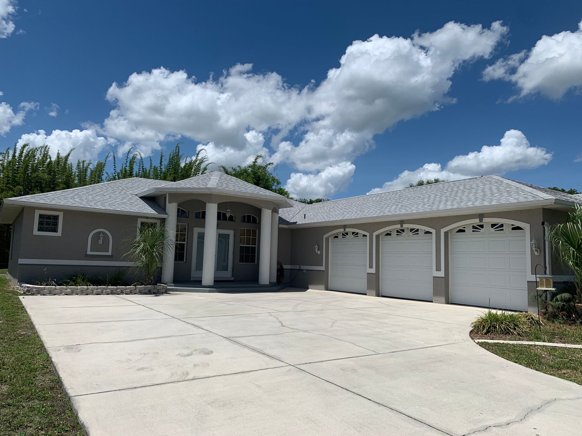 Single-story house with three-car garage, wide driveway, and cloudy blue sky