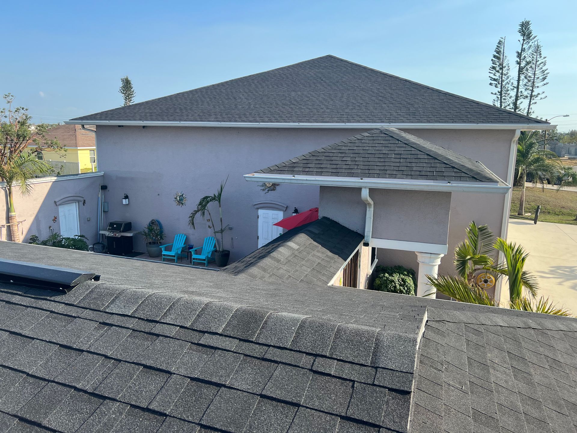 Rooftops of a suburban home with a gray shingle roof and a small covered patio in bright daylight
