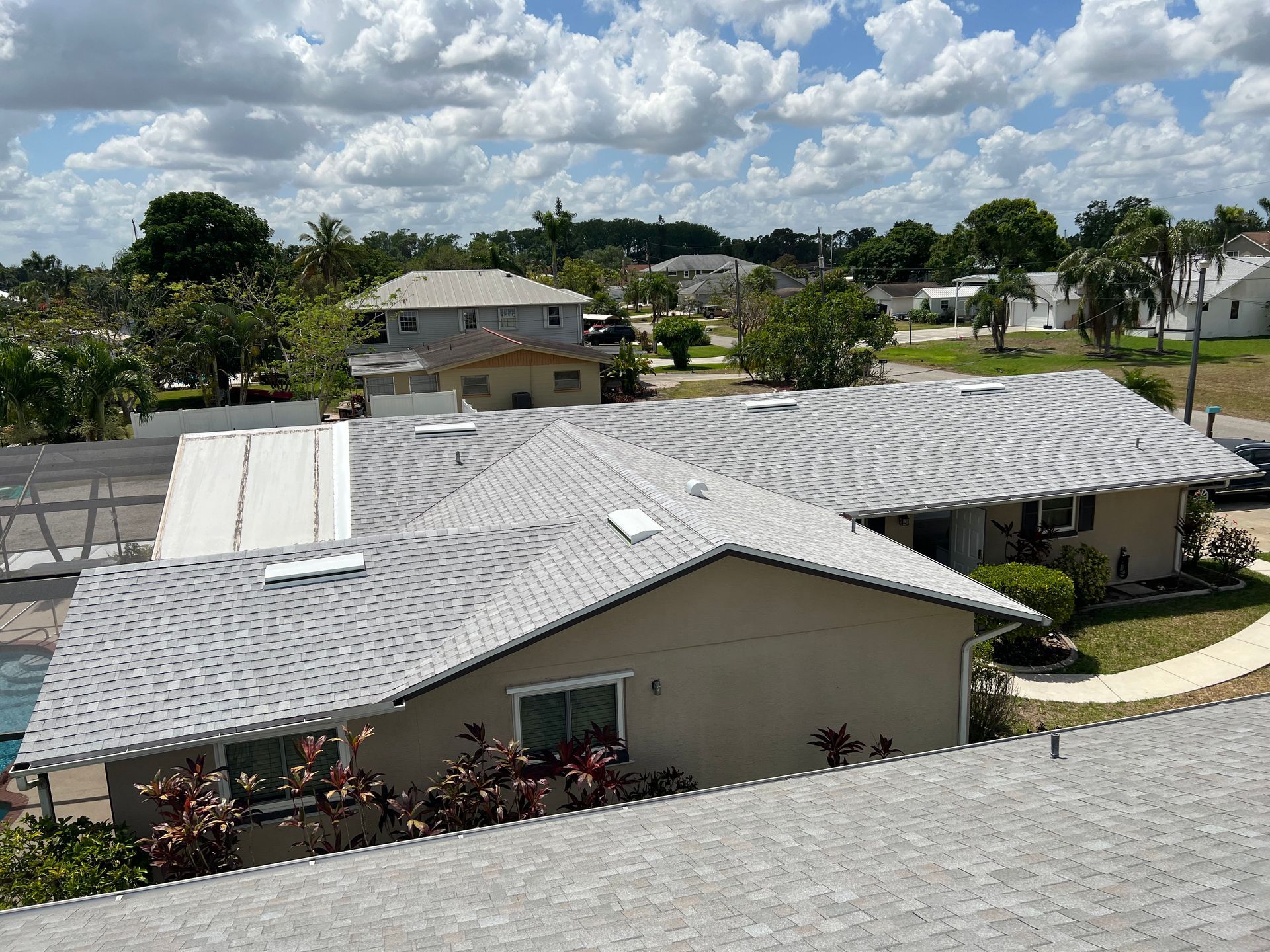Residential neighborhood with gray shingle roofs under a partly cloudy sky