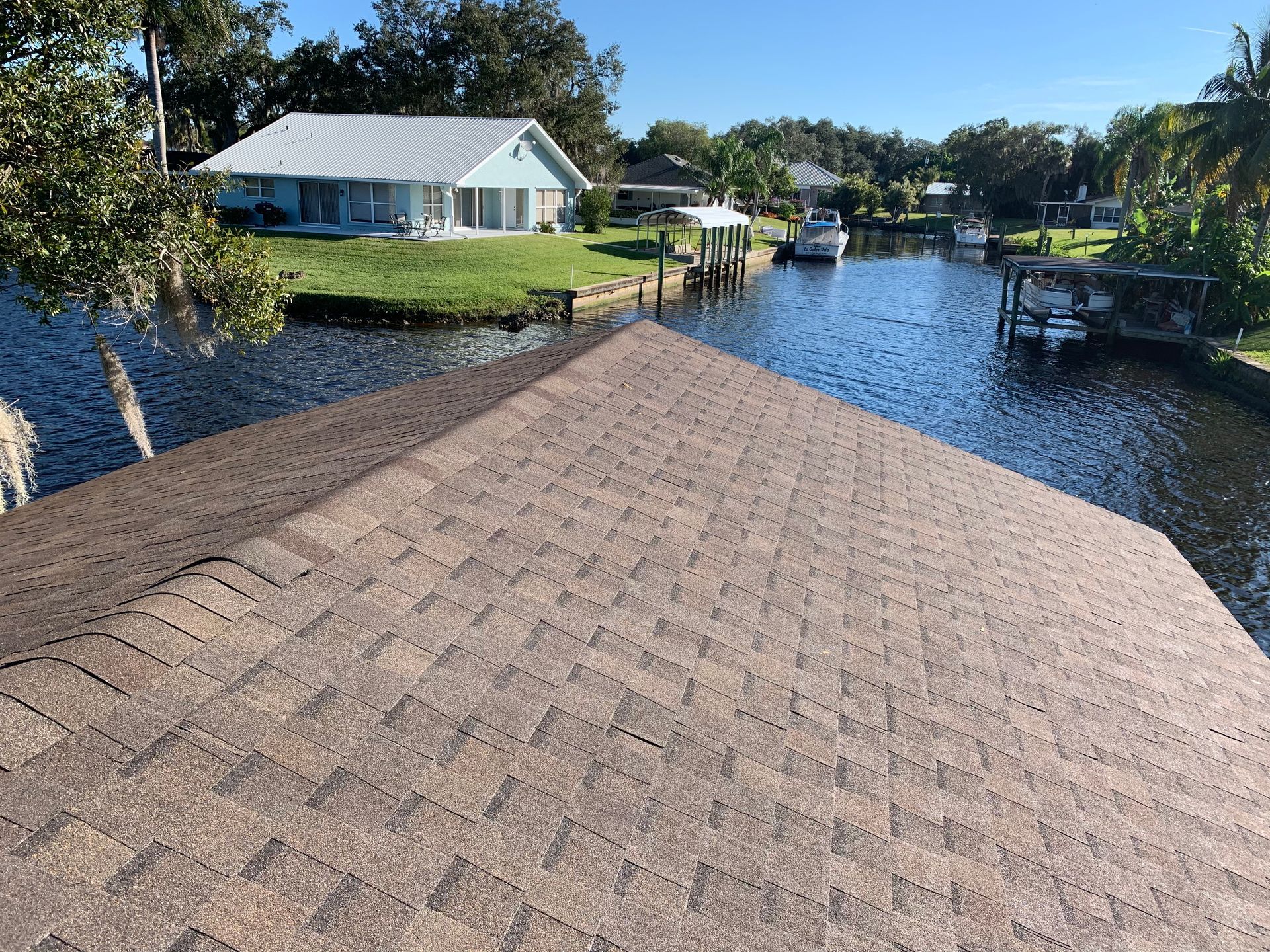 Roof view over a canal with a white house, dock, and boats on a sunny day