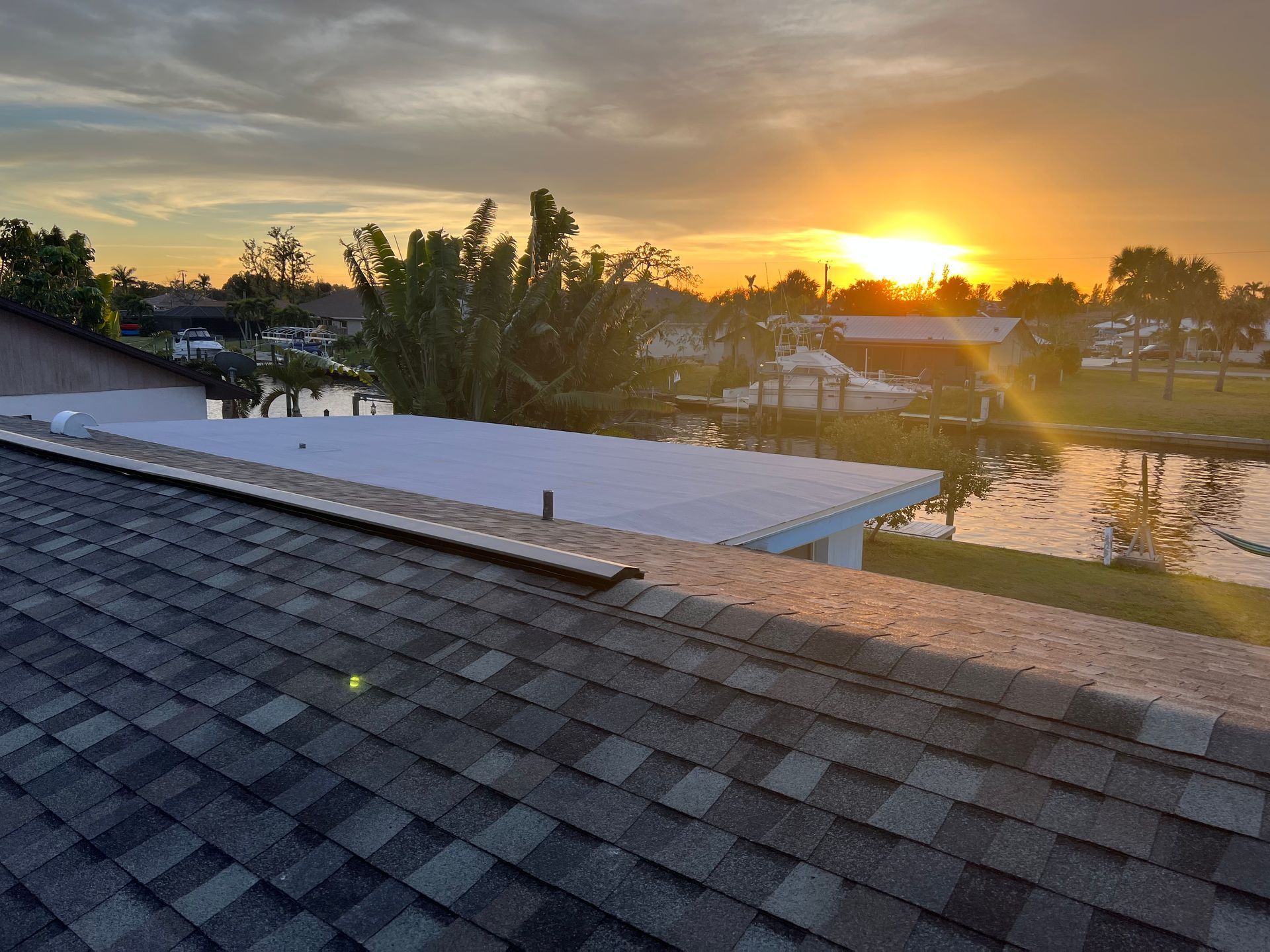 Sunset over a canal with trees, a roof in the foreground, and warm golden light reflecting on the water