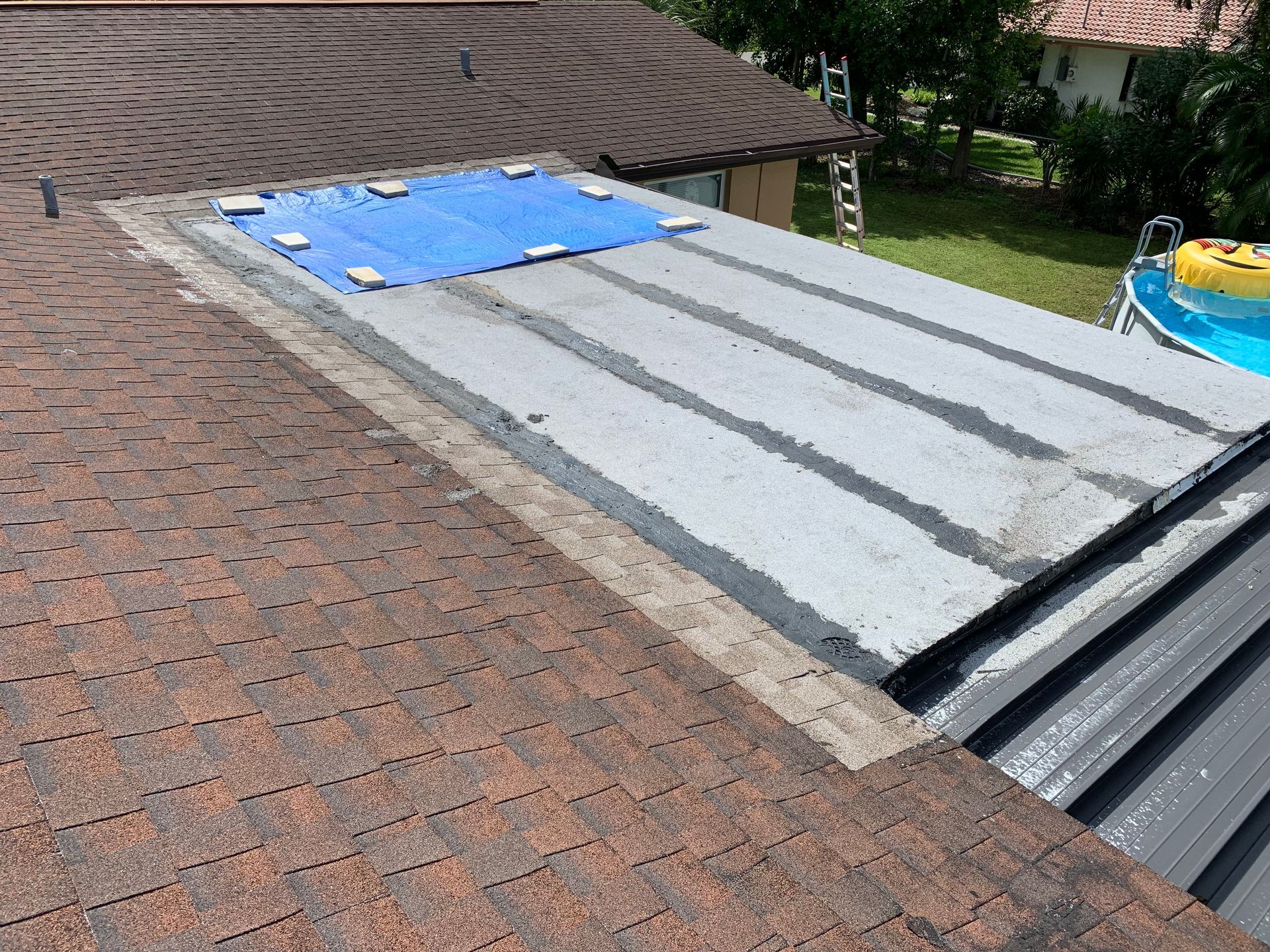 Rooftop with a gray membrane section, blue tarp, and brown shingles on a house roof