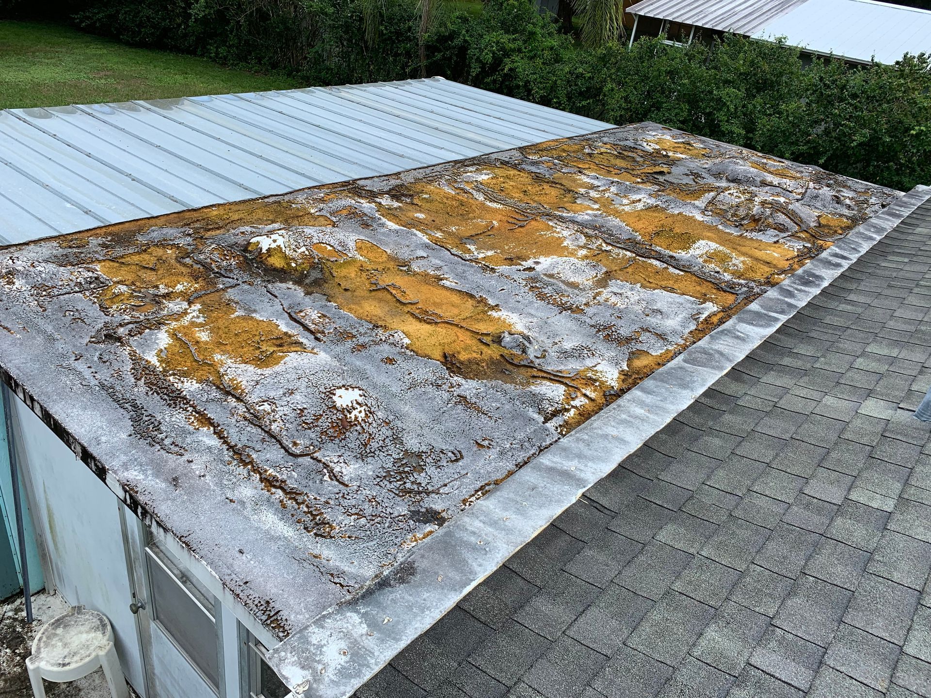 Aerial view of a weathered roof with patches of moss and discoloration beside a shingled roof.