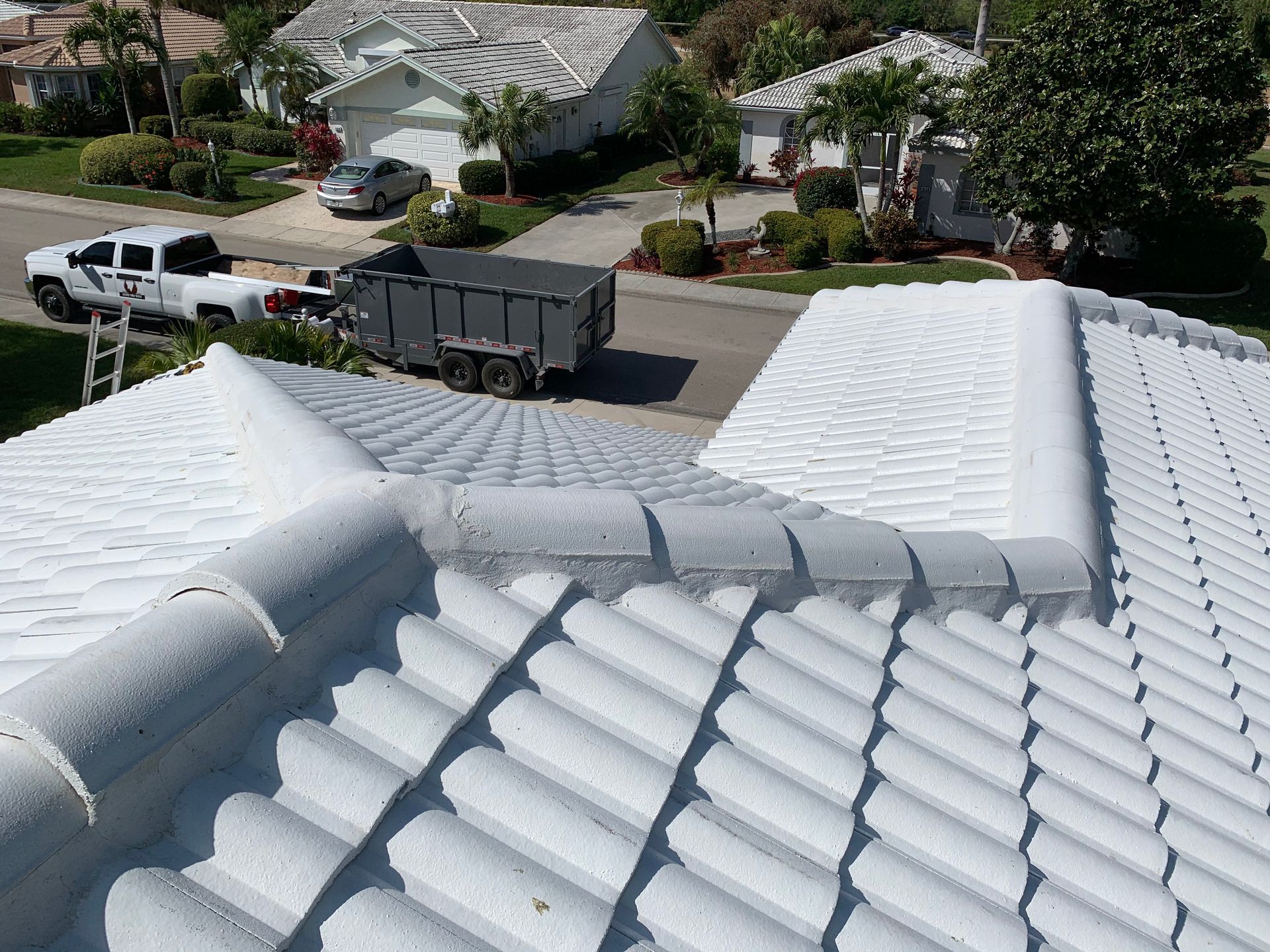 View from a tiled roof onto a suburban street with a white pickup and a gray dumpster truck parked below