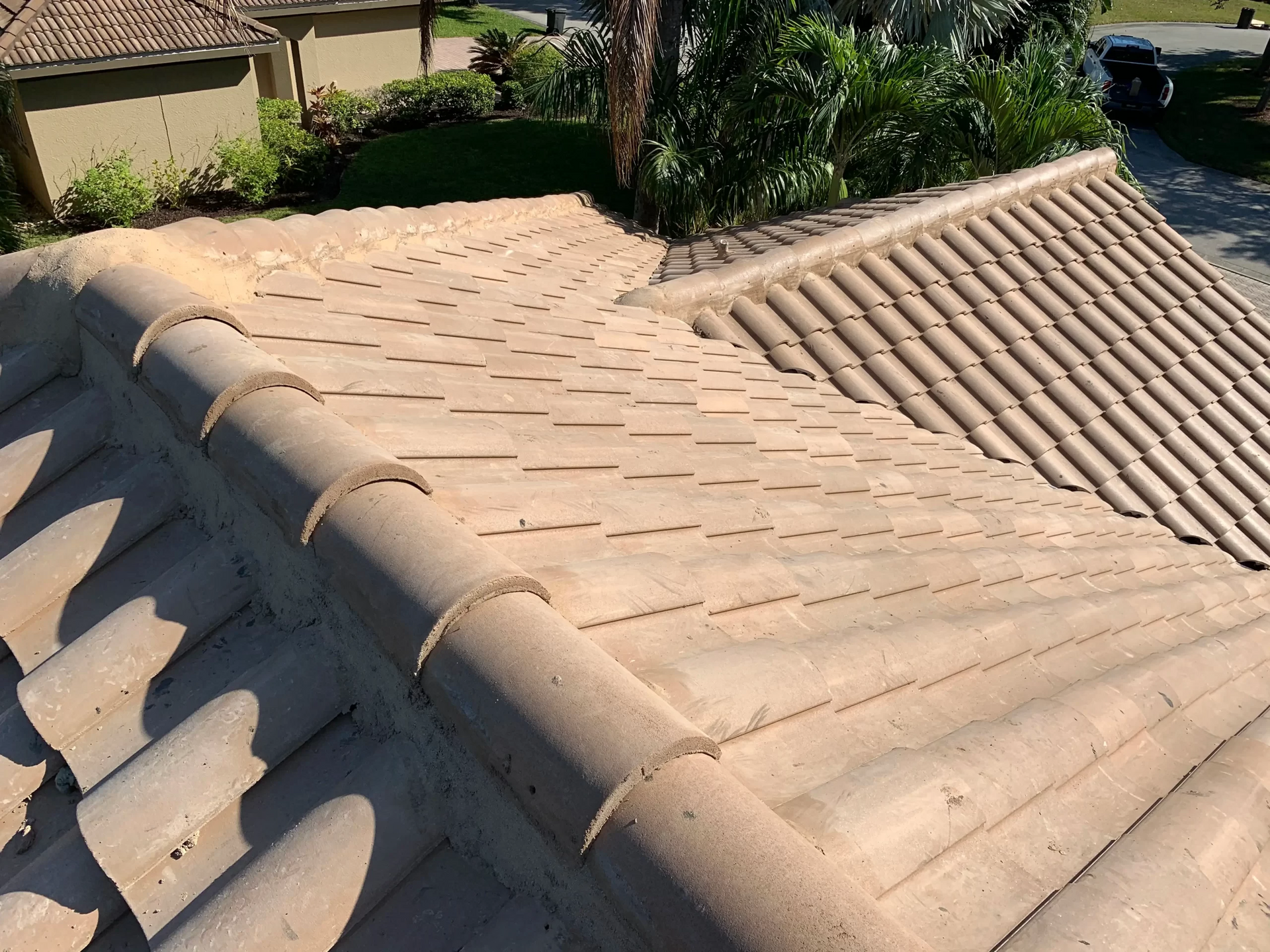 Beige tiled roof with a ridge line and neighboring roof sections in sunlight