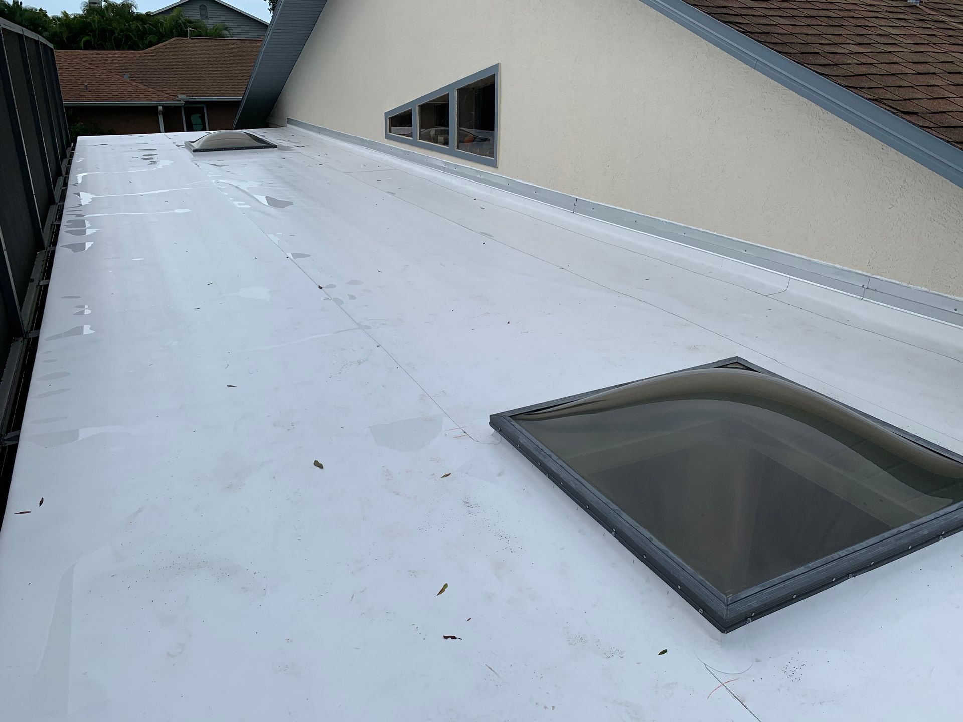 Flat white roof with a skylight next to a building wall and trees in the background