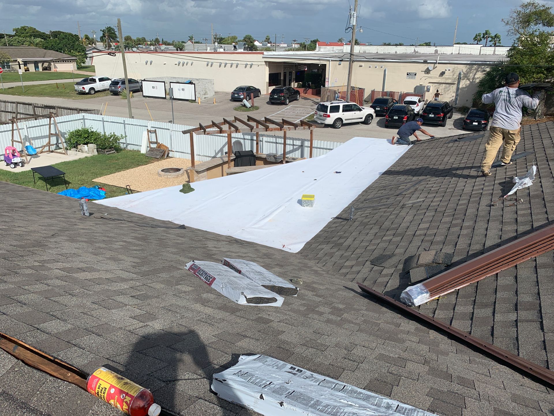Rooftop with a large white tarp, workers, and construction materials scattered across a flat roof
